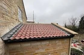 Corner of a building with a red tiled roof and a stone wall, overcast sky.