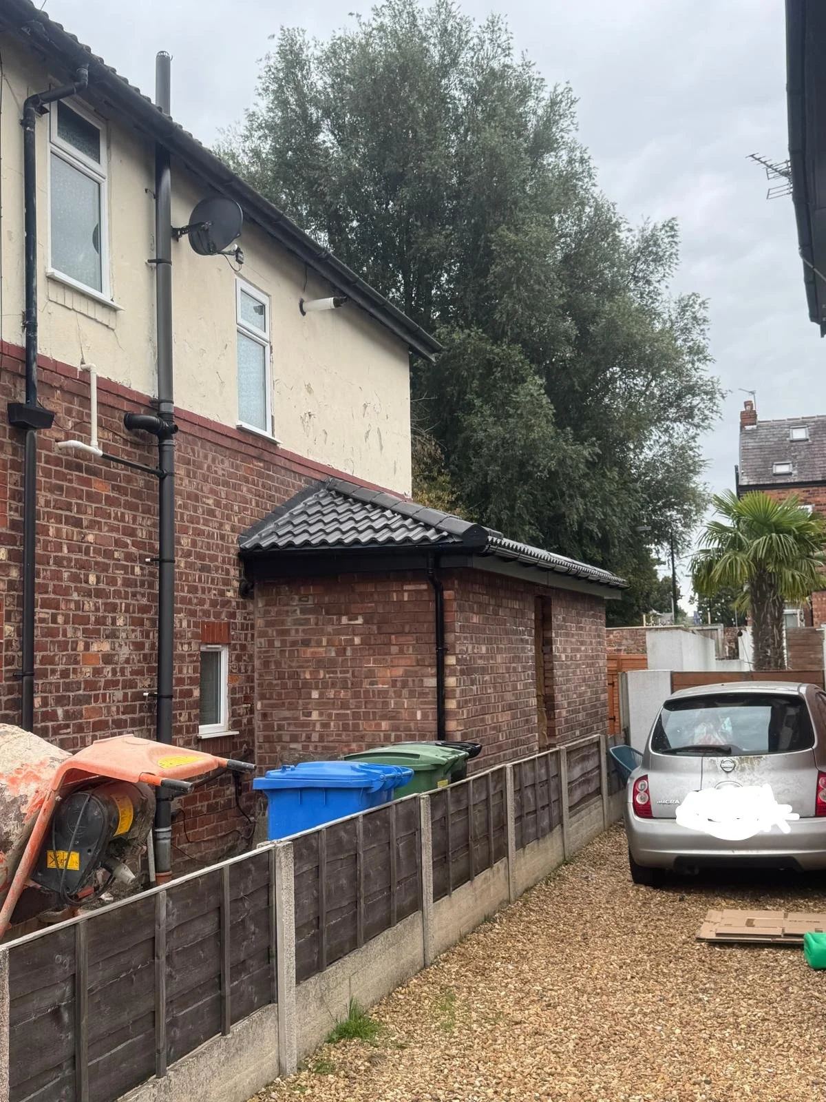 Backyard with a brick wall, garage, parked car, trees, and outdoor equipment.
