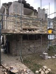 A building under renovation with scaffolding around it, showing a partially constructed second floor or roof structure.