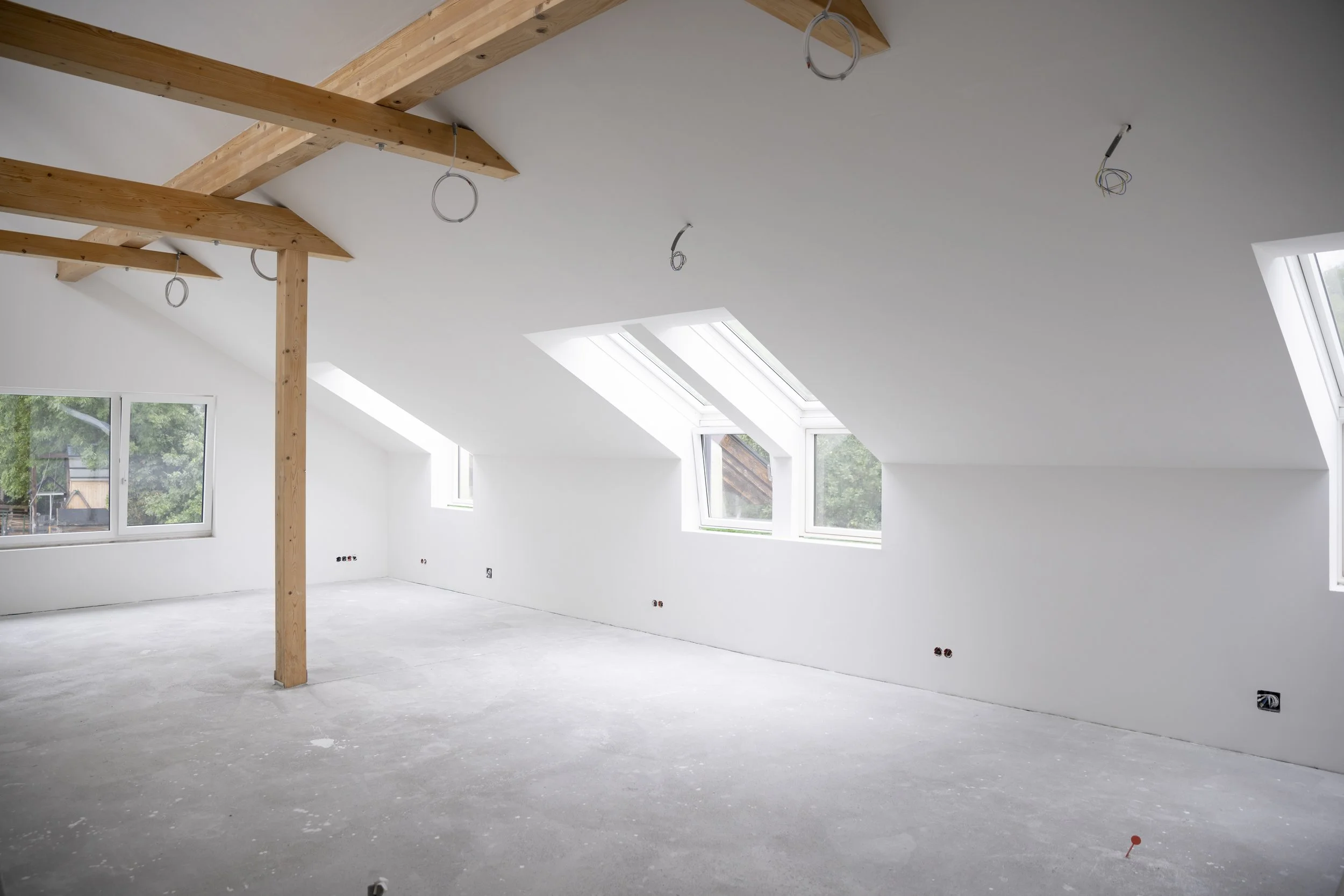 A converted loft space with white walls, large windows, and exposed wooden beams on the ceiling.