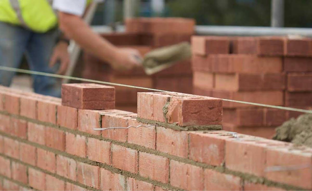 Construction worker building a brick wall with mortared bricks on a construction site.
