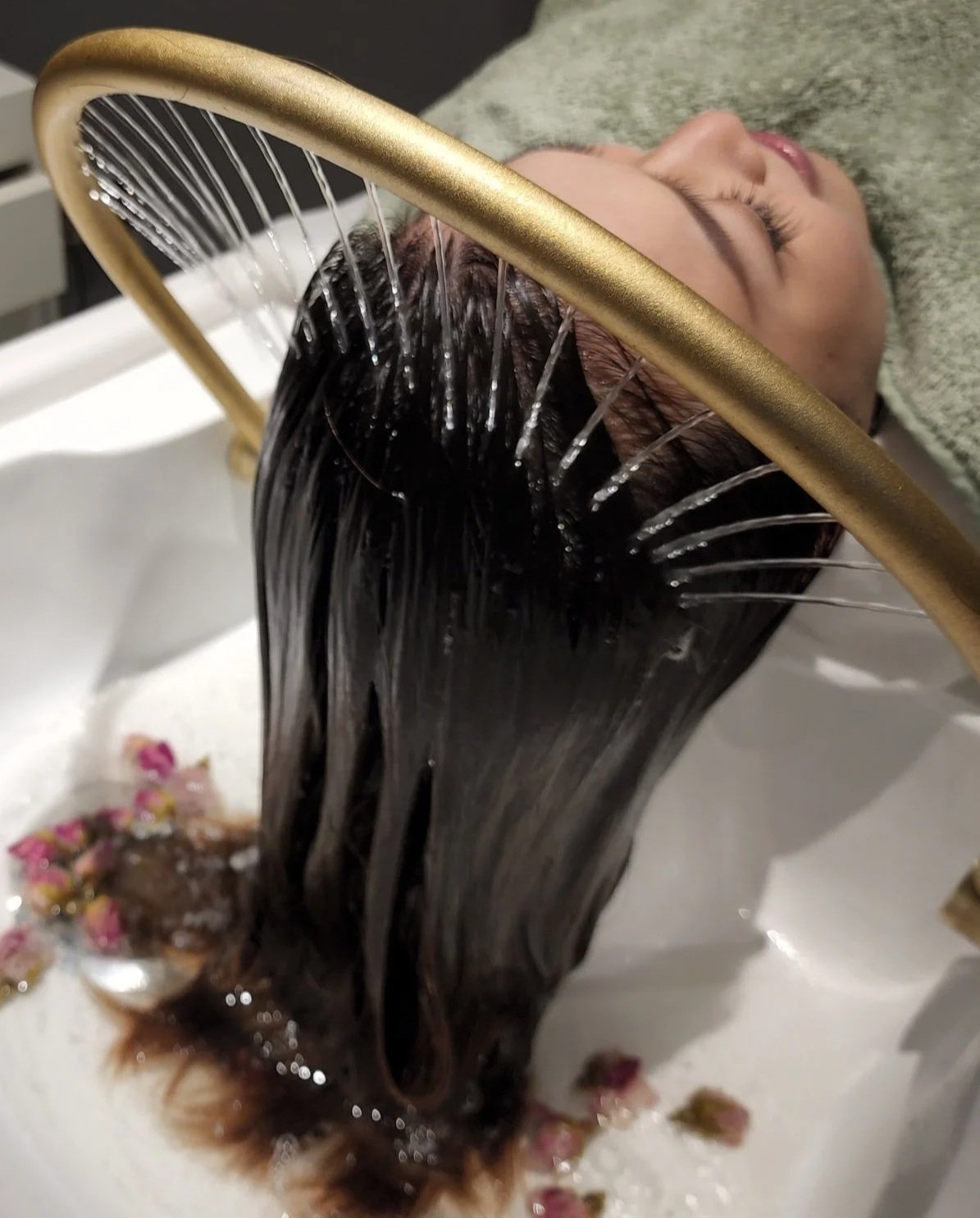 A person with their hair washed and covered with shampoo, lying back with eyes closed, in a salon or spa setting.