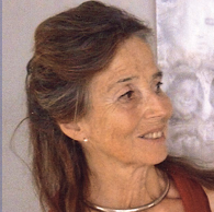 Nahaufnahme einer lächelnden älteren Frau mit braunen Haaren, die nach rechts blickt, im Hintergrund eine weiße Statue.