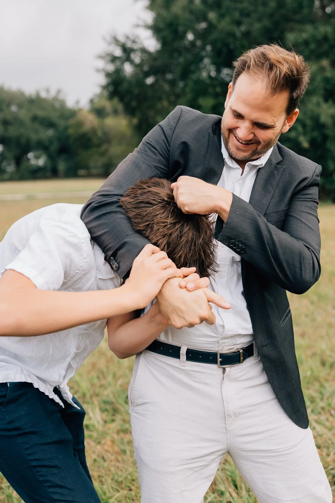 Two men engaged in a playful mock fight outdoors, with one man wearing a gray suit fighting the other in a white shirt.