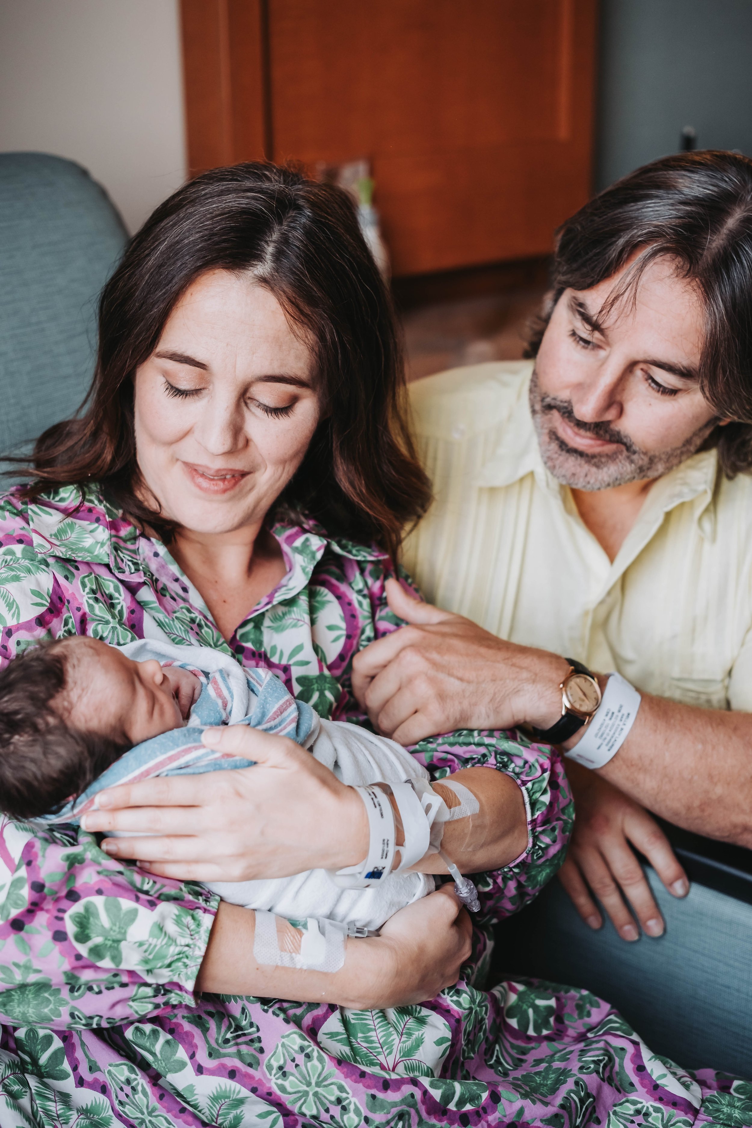 Mother holding a newborn baby in an Alaskan hospital room, with father looking on lovingly