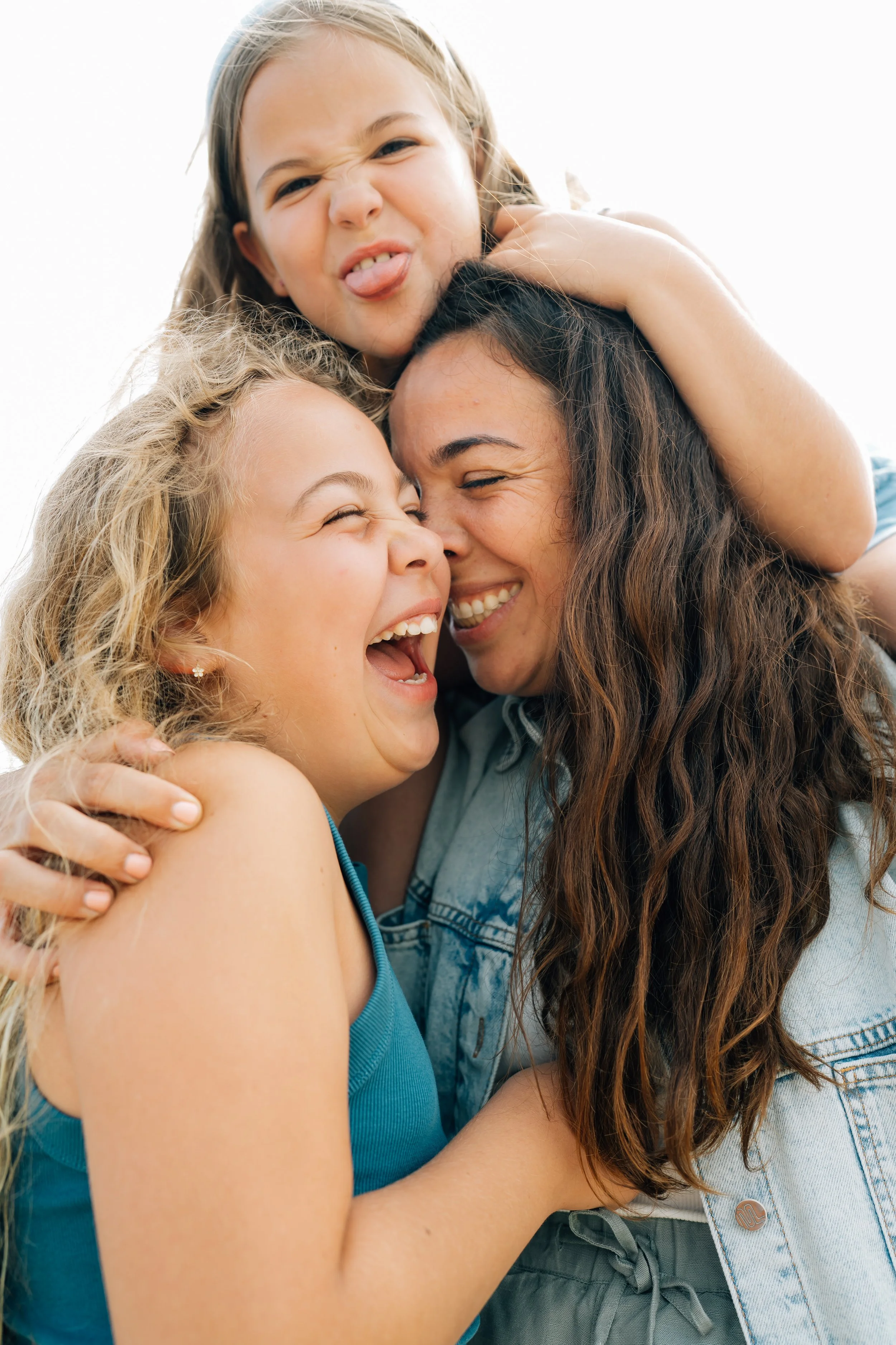 A woman and two young girls sharing a joyful, playful moment outdoors, with smiles and laughter.
