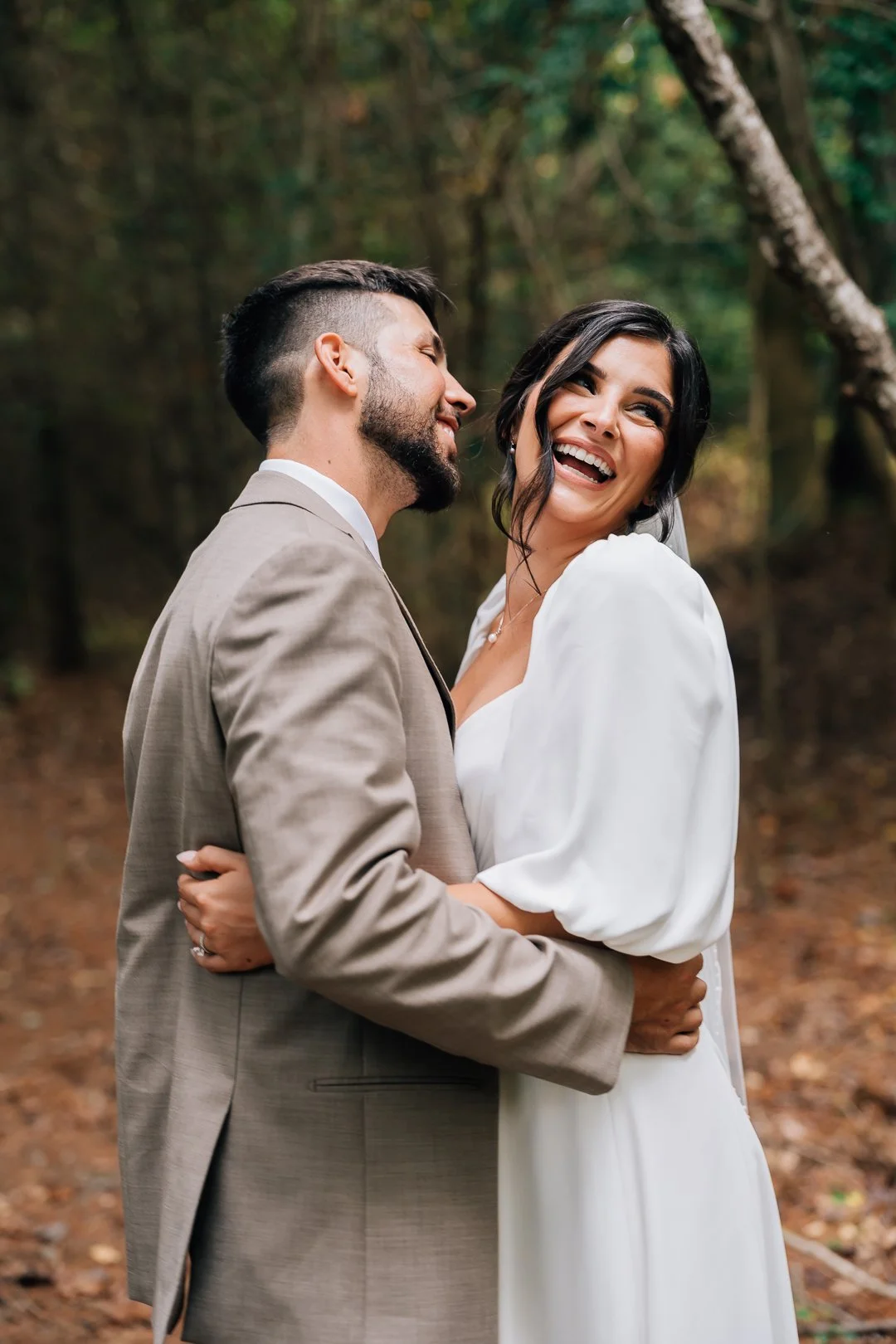 bride smiles off her shoulder as groom tries to kiss her in the forest in juneau alaska