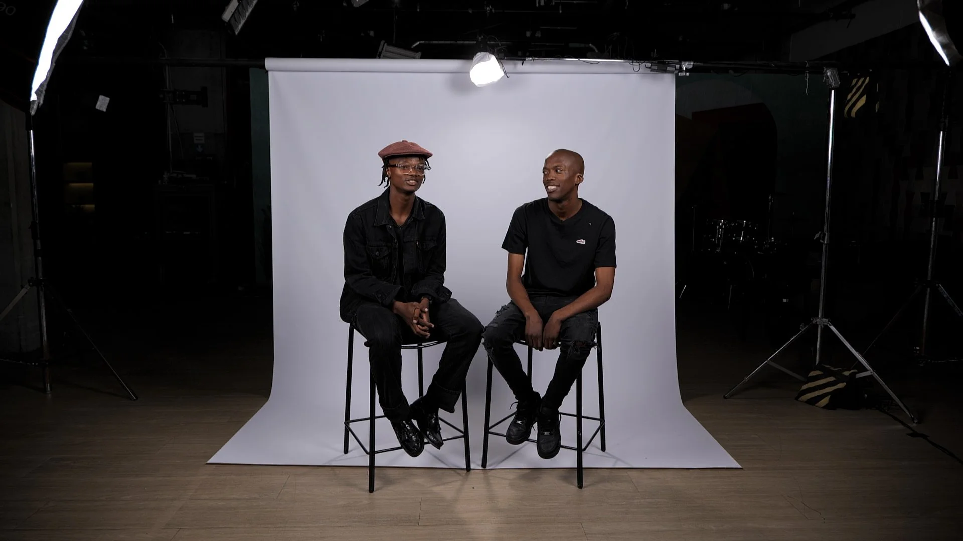 Culthos Employer Branding, Two employees sitting on high stools against a white backdrop in a photography studio, with lighting equipment visible around them.