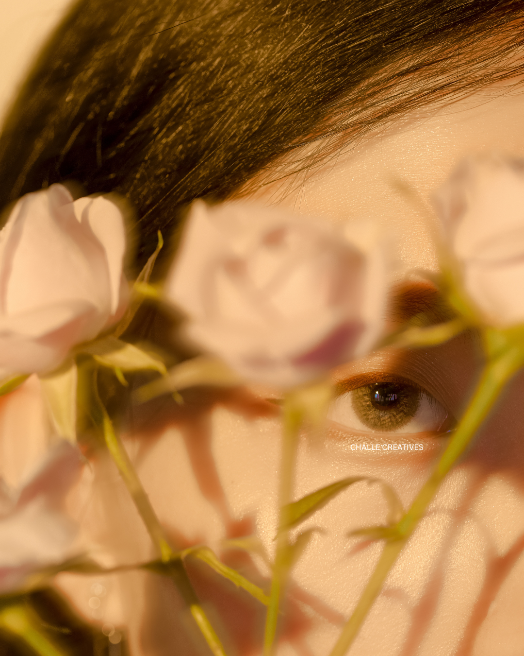 Close-up of a woman's face partially obscured by pink flowers, with visible eye and dark hair.