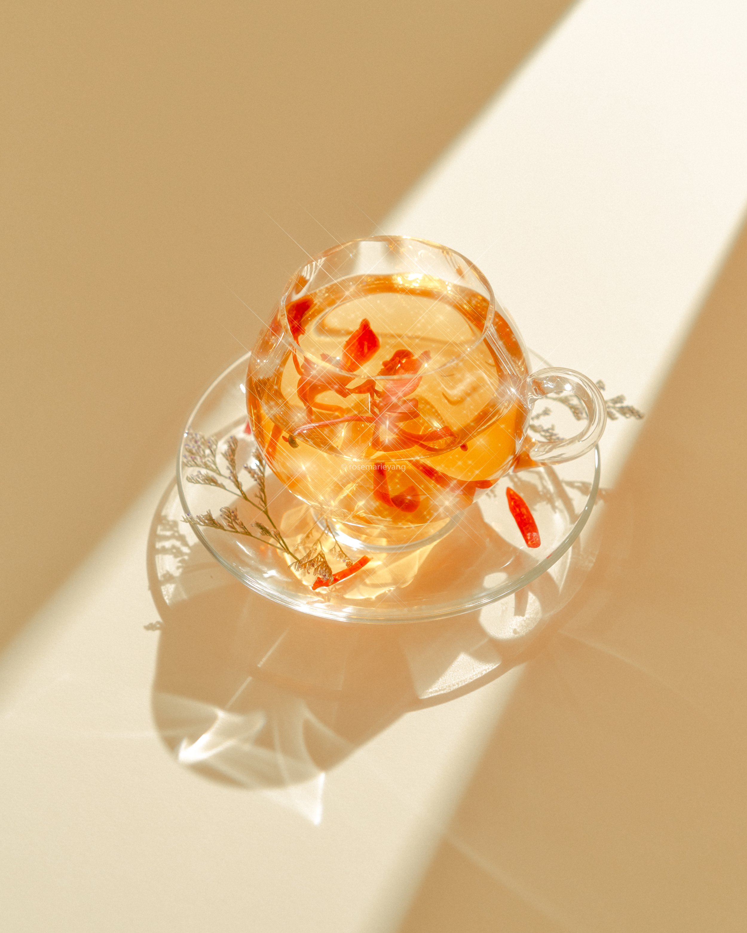 A glass teacup with tea and slices of red chili peppers on a glass saucer, casting a shadow on a white surface with sunlight.