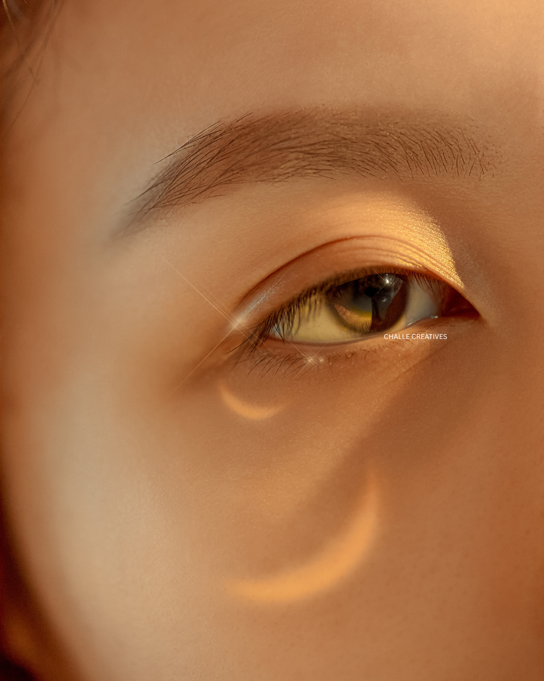 Close-up of a person's eye with makeup and a soft glow reflection on the skin.