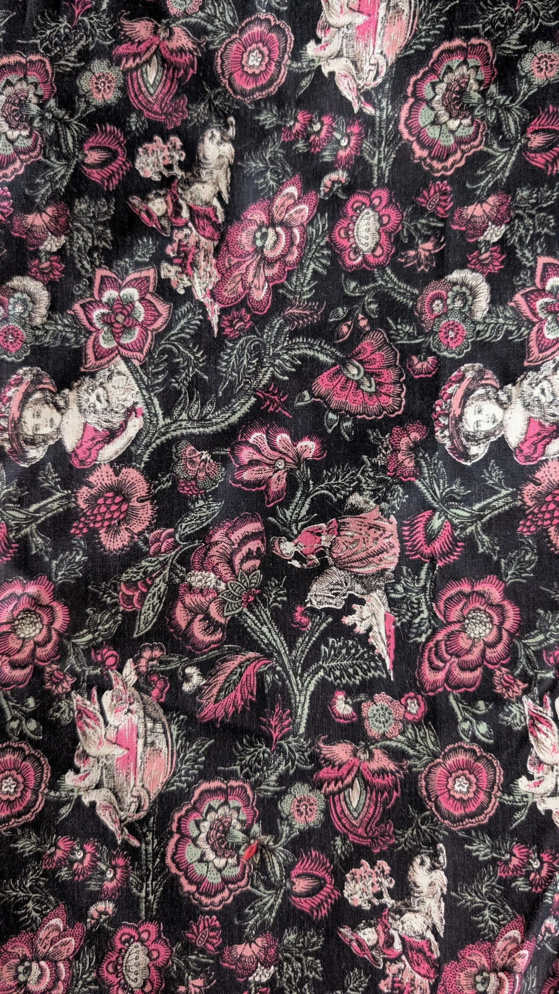 A textile pattern featuring pink, white, and green floral designs with small illustrations of people and animals on a black background.