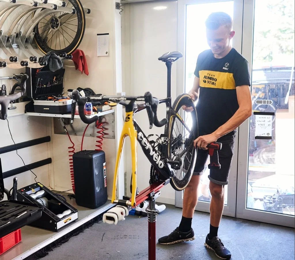 een man die een fiets op een reparatiestandaard onderhoudt in een fietsenwinkel of werkplaats.