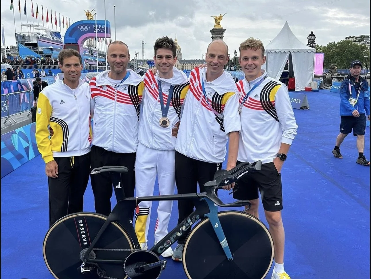 Vijf olympische atleten in gouden medaille op het nek, samen met een fiets, poseren voor een foto na een wedstrijd op de Olympische Spelen Parijs 2024.