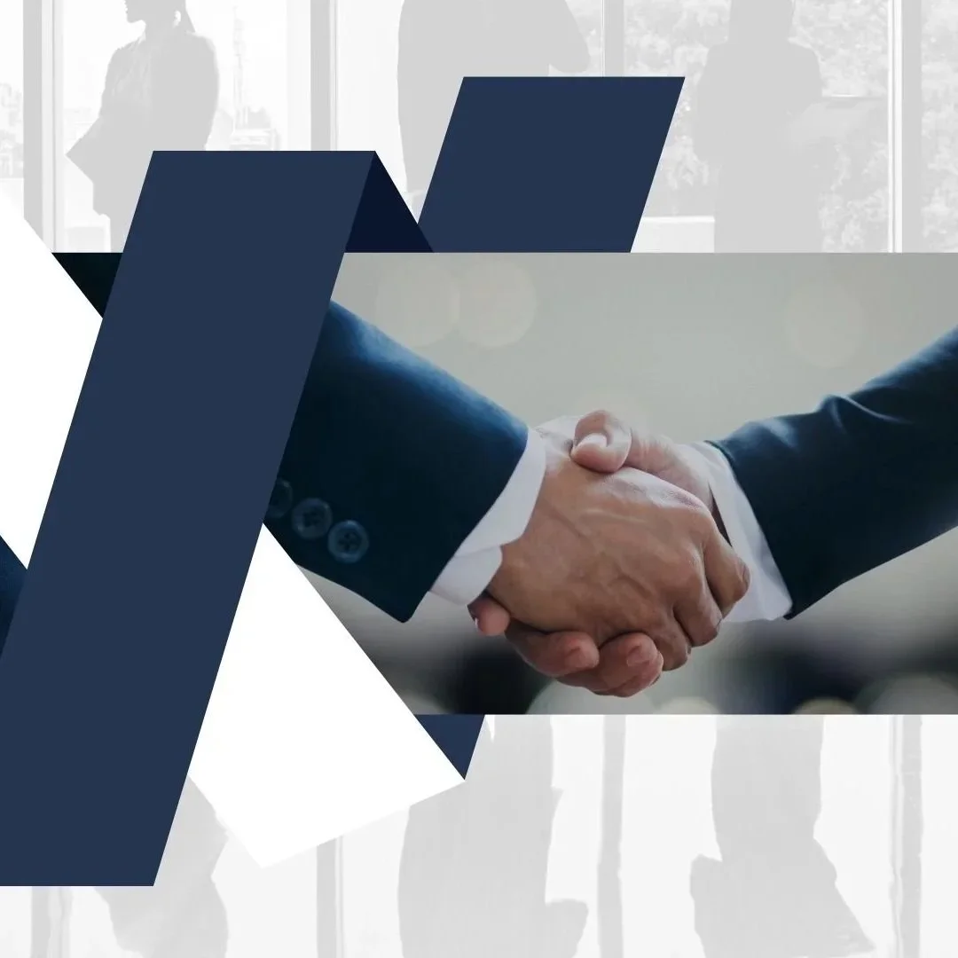 Close-up of two people shaking hands, with a background of office windows and silhouettes of people.