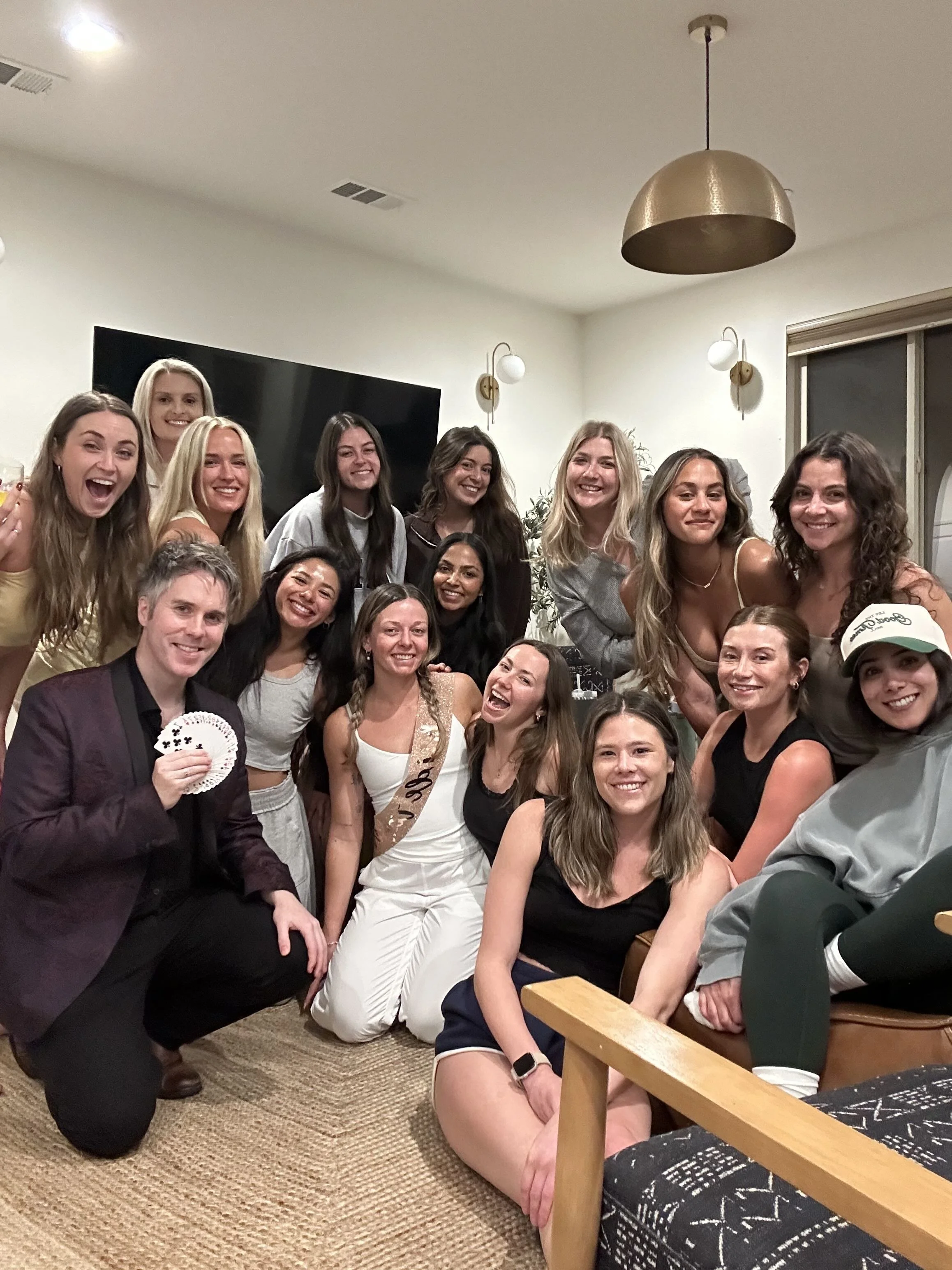 Group of people celebrating, some holding playing cards, gathered indoors with smiles and happy expressions.