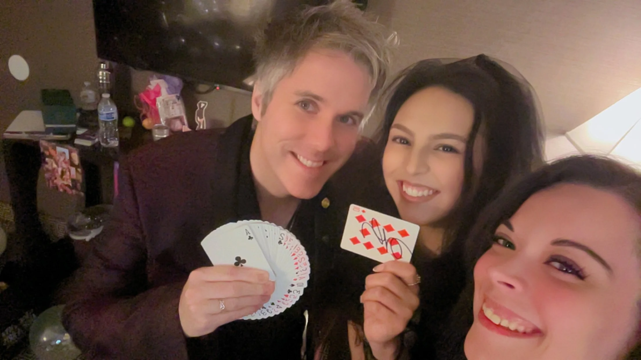 Three women celebrating and holding playing cards, smiling and enjoying a social gathering in a dimly lit room.