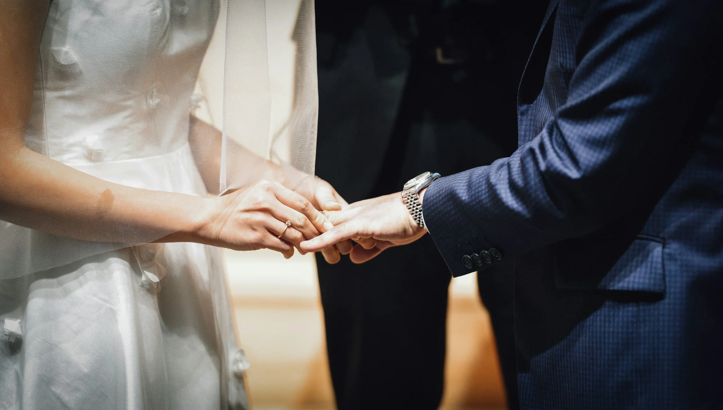 A bride and groom holding hands during their wedding ceremony, with the bride wearing a white dress and the groom in a dark suit.
