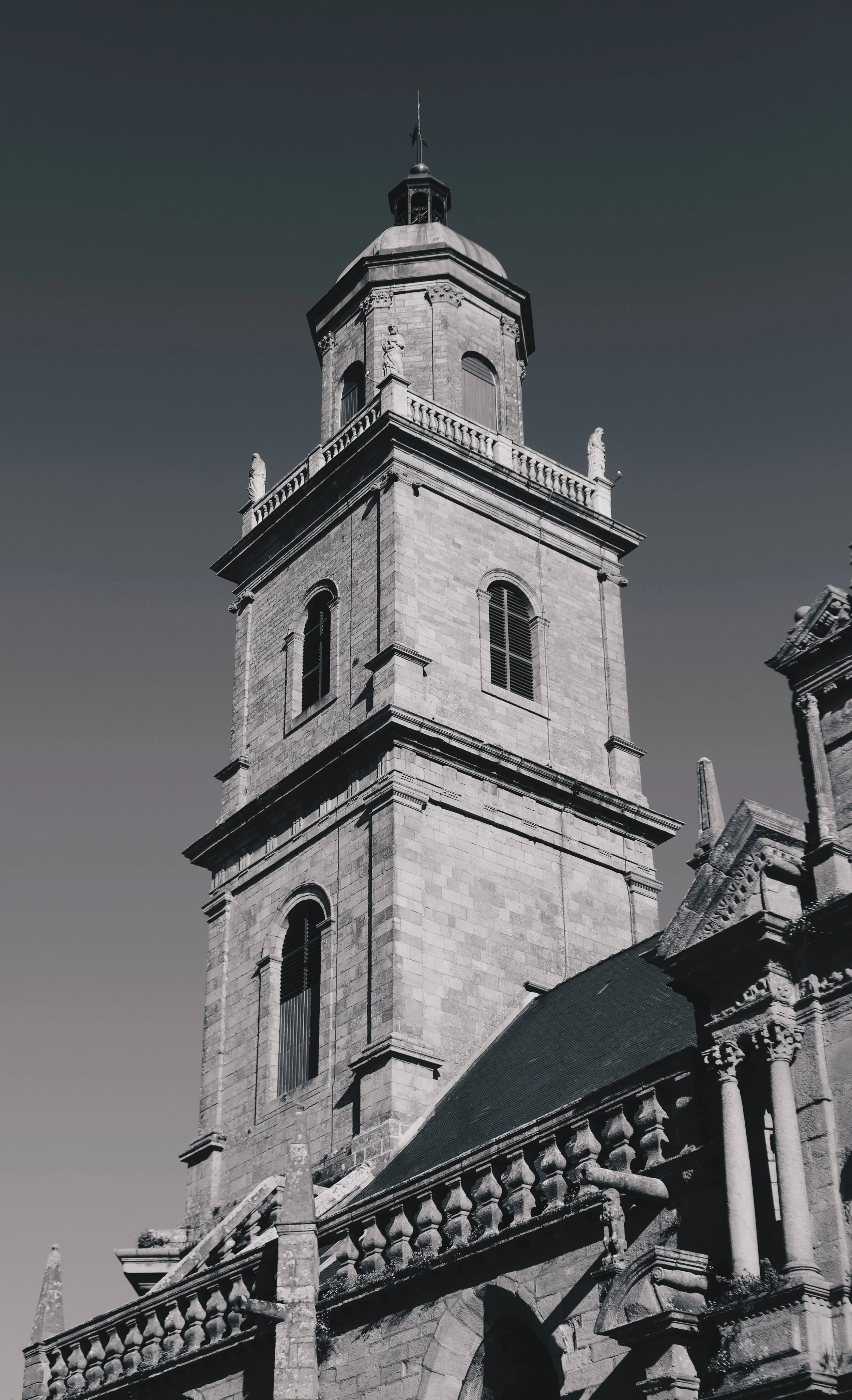 Tour d'église en pierre avec horloge et balcon, ciel clair en arrière-plan.