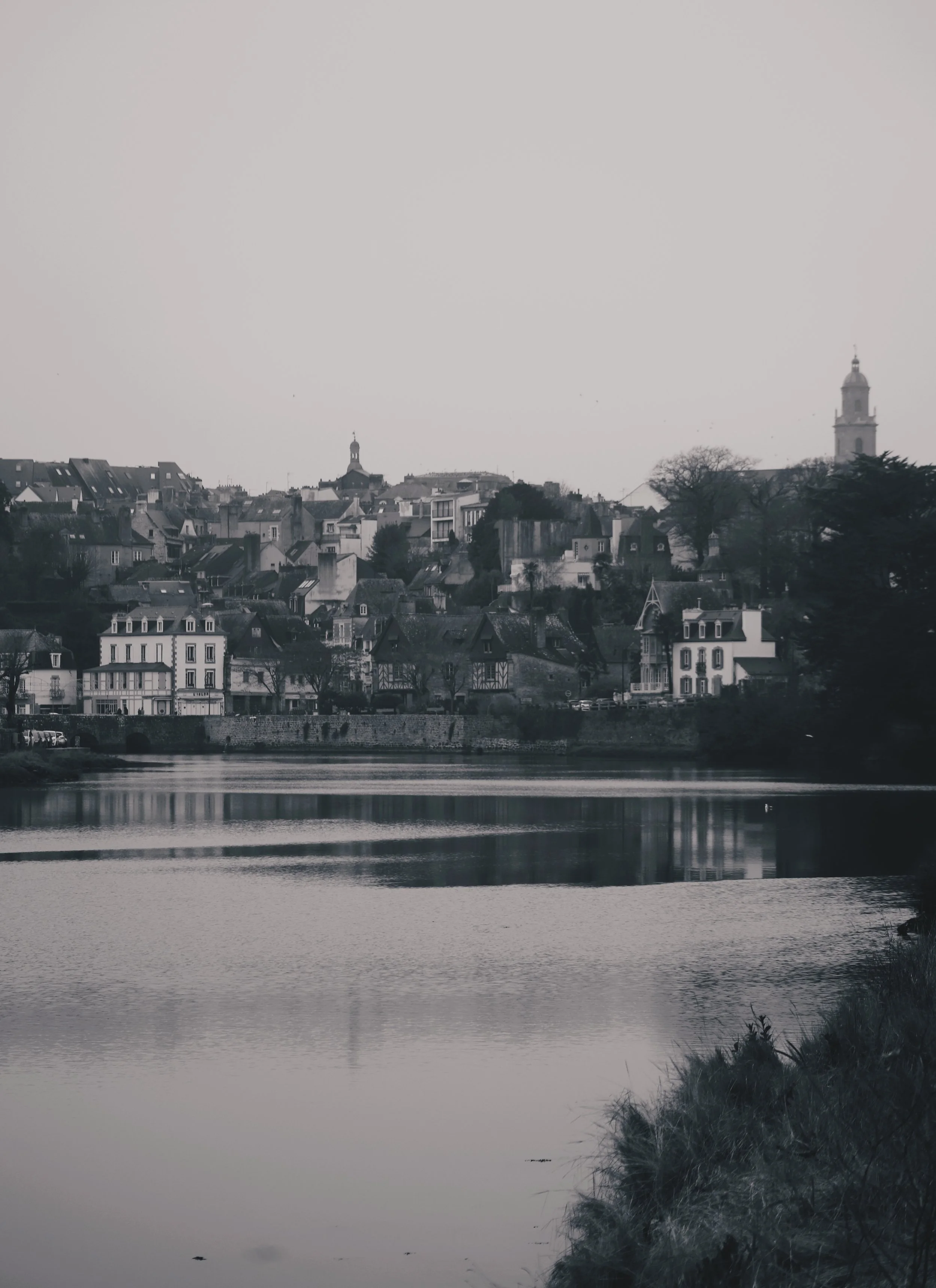Une vue d'une ville avec des bâtiments anciens et modernes le long d'une rivière, en noir et blanc.