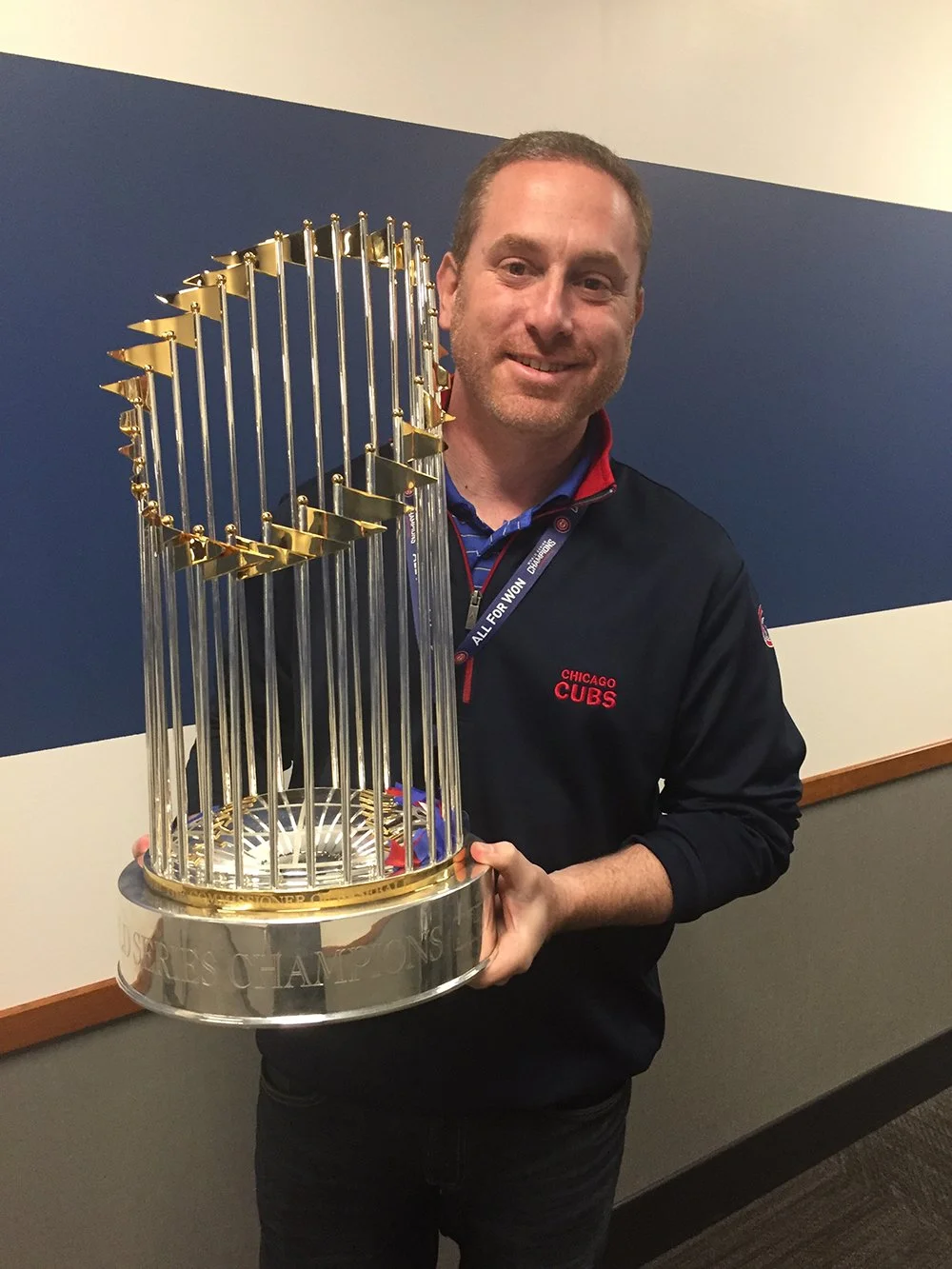 A man smiling and holding the Stanley Cup trophy, wearing a black Chicago Cubs jacket.