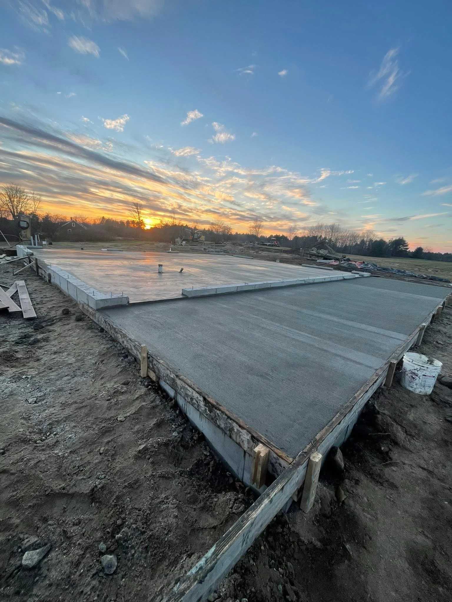 Concrete slab foundation on a construction site during sunset with a partly cloudy sky.
