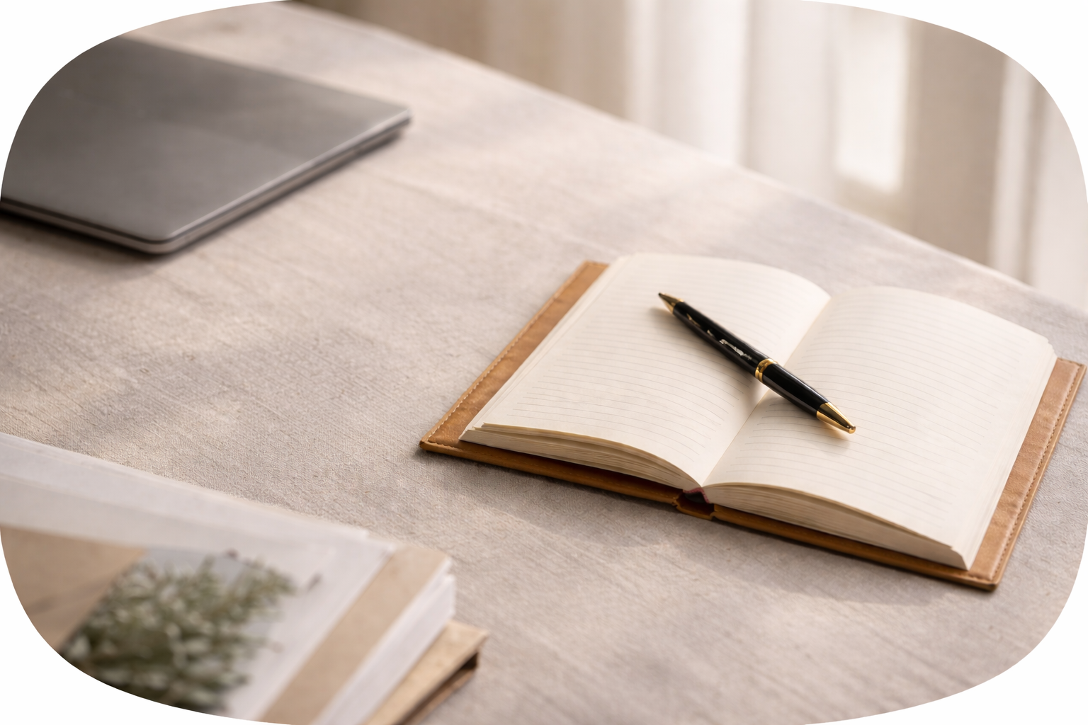 Open notebook with lined pages and a black and gold pen resting on it, on a beige table with a closed laptop in the background.