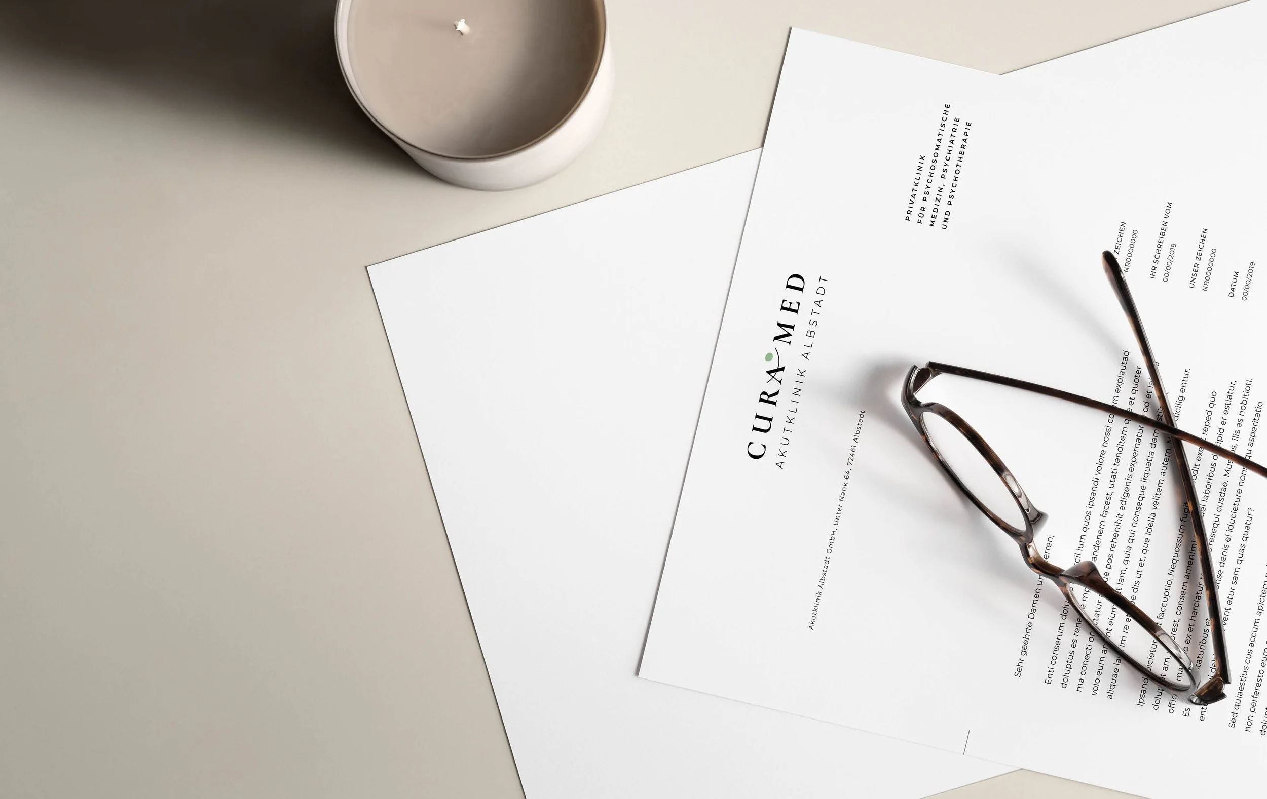 A white desk with a candle, a pair of glasses, and two documents about a medical clinic, with one document partially covering the other.