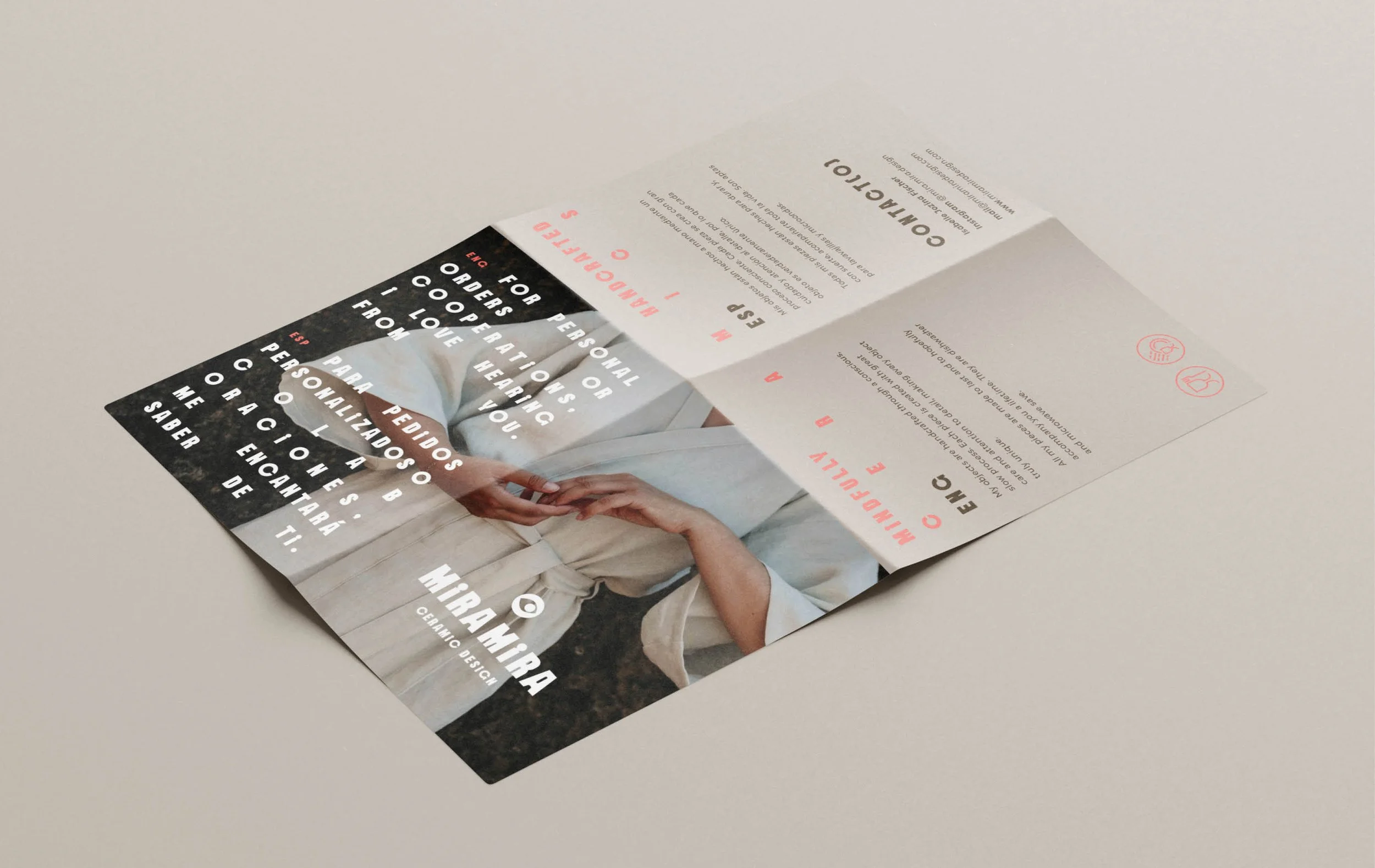 A folded brochure or flyer on a plain surface, featuring a person in a beige outfit with hands at the center. The brochure has text in multiple languages and includes icons for contact information.