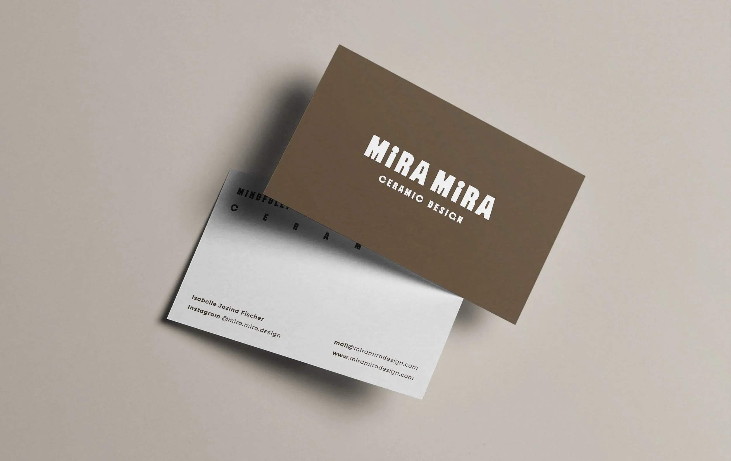 Close-up of business cards on a light surface, one brown with white text and one white with black text, featuring names, contact details, and design branding.