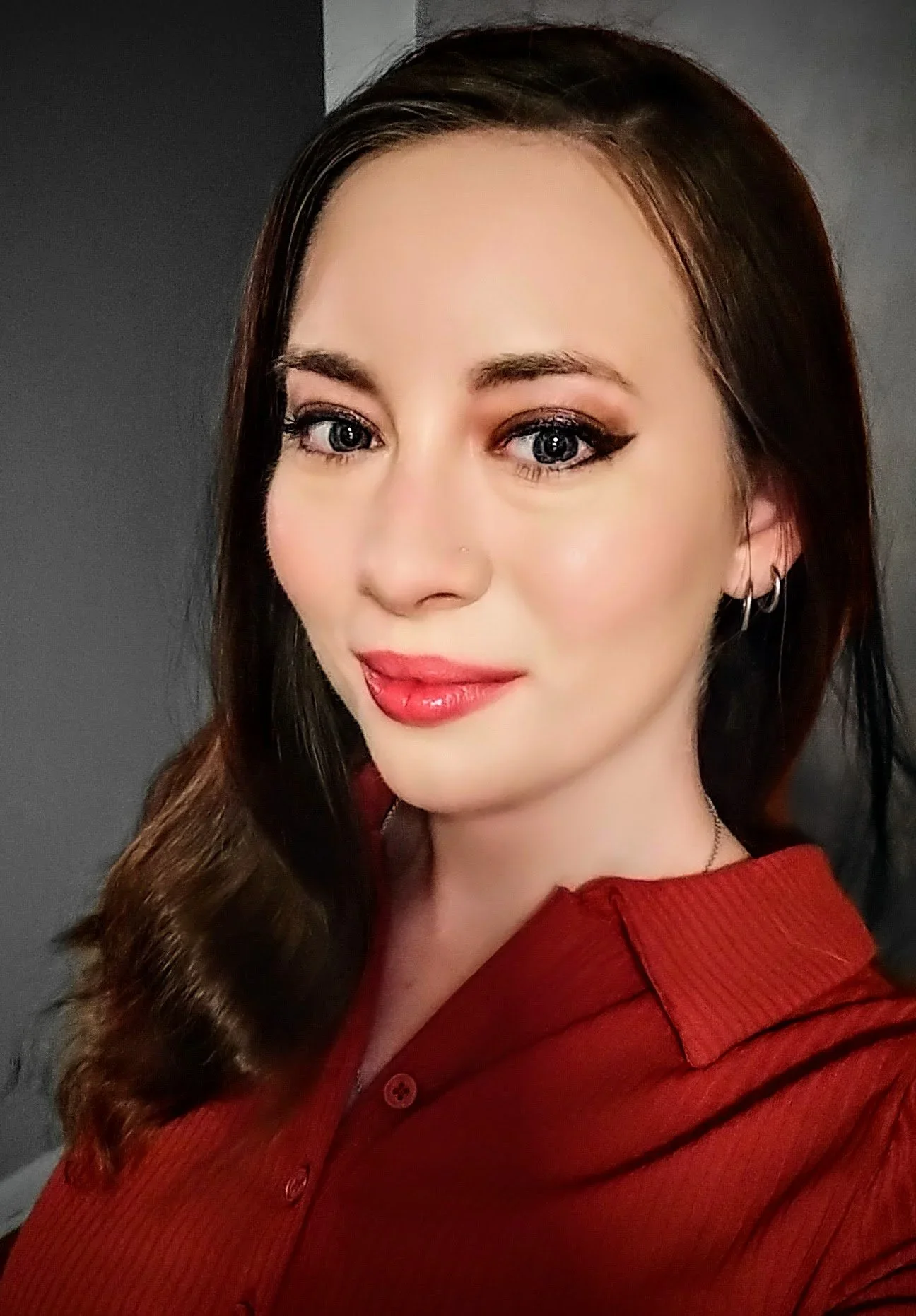 A woman with blue eyes and brown hair, wearing red lipstick and a red shirt, smiling for a close-up photo.