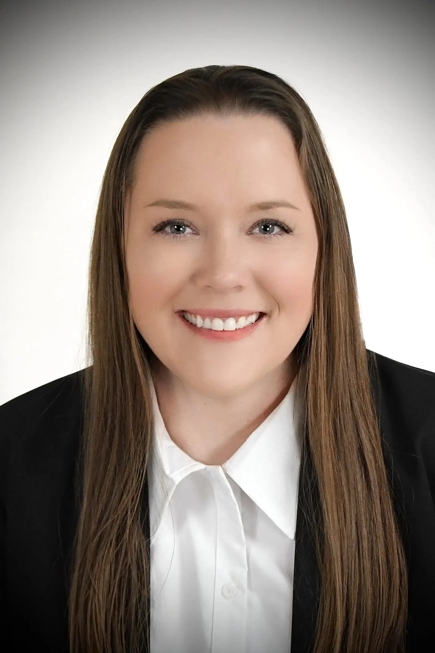 A woman with long brown hair, smiling, dressed in a black blazer and white collared shirt, against a light gradient background.