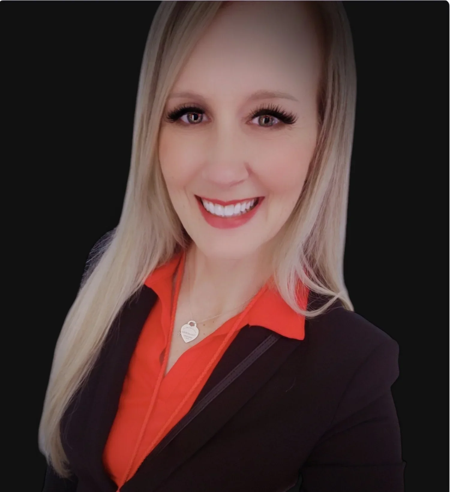 Portrait of a smiling woman with blonde hair, wearing a red shirt and black blazer, against a black background.