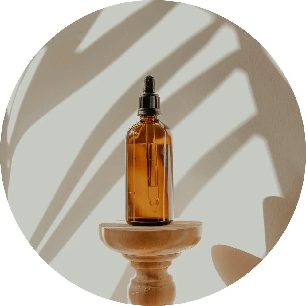 Amber glass dropper bottle on a wooden pedestal with shadows of leaves cast on the wall behind it.