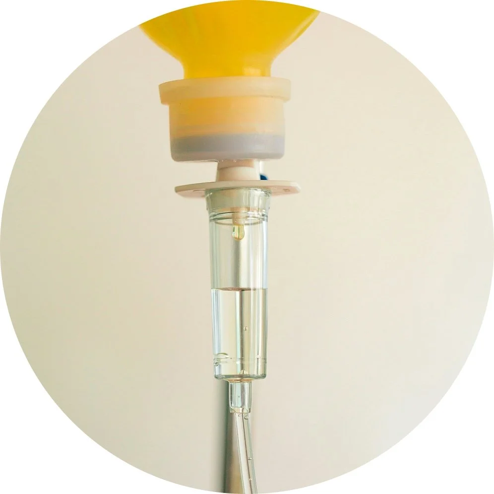 Close-up of a medical IV drip setup with a yellow IV bag, tubing, and a fluid bag, against a plain background.