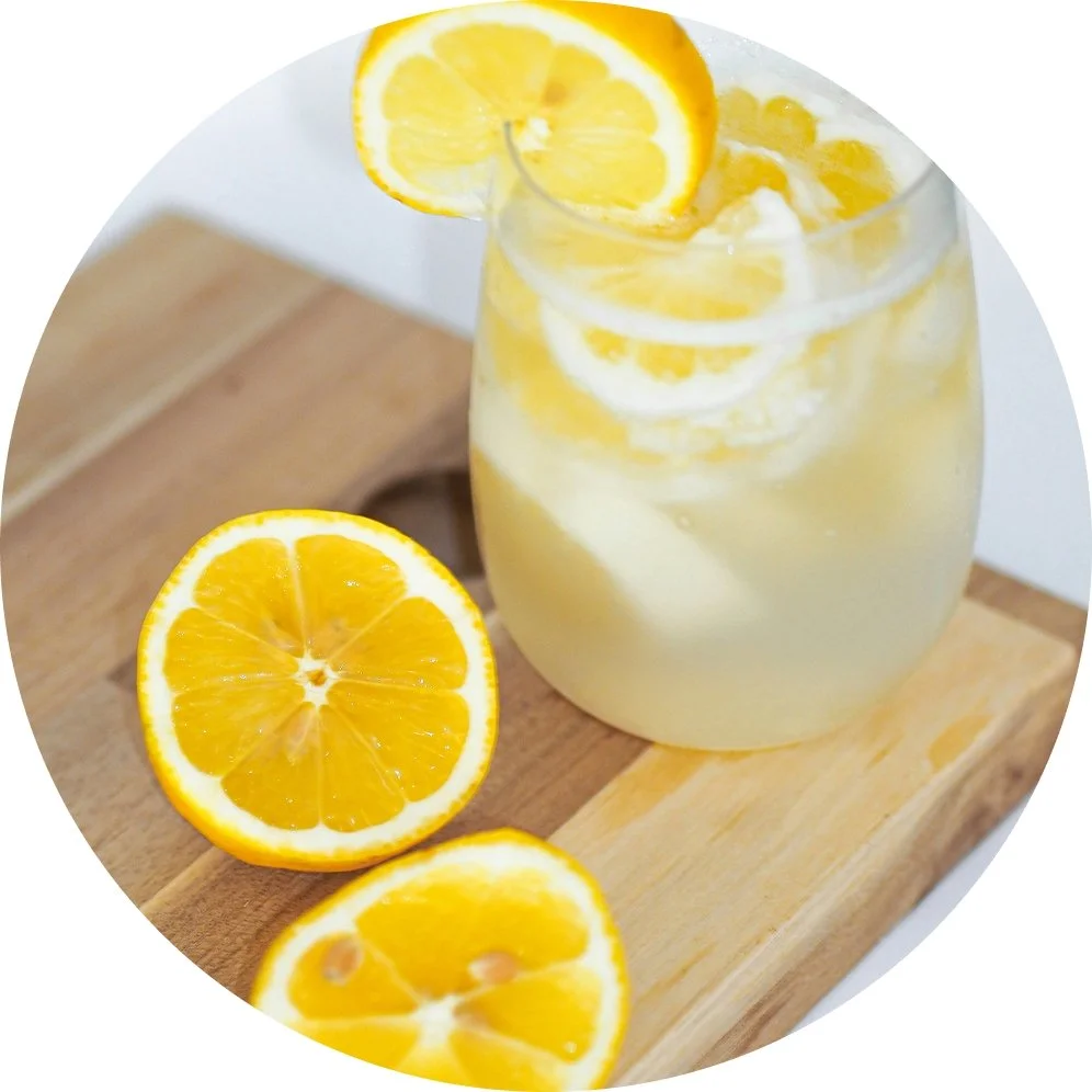 A glass of lemonade with lemon slices and a lemon half on a wooden cutting board.