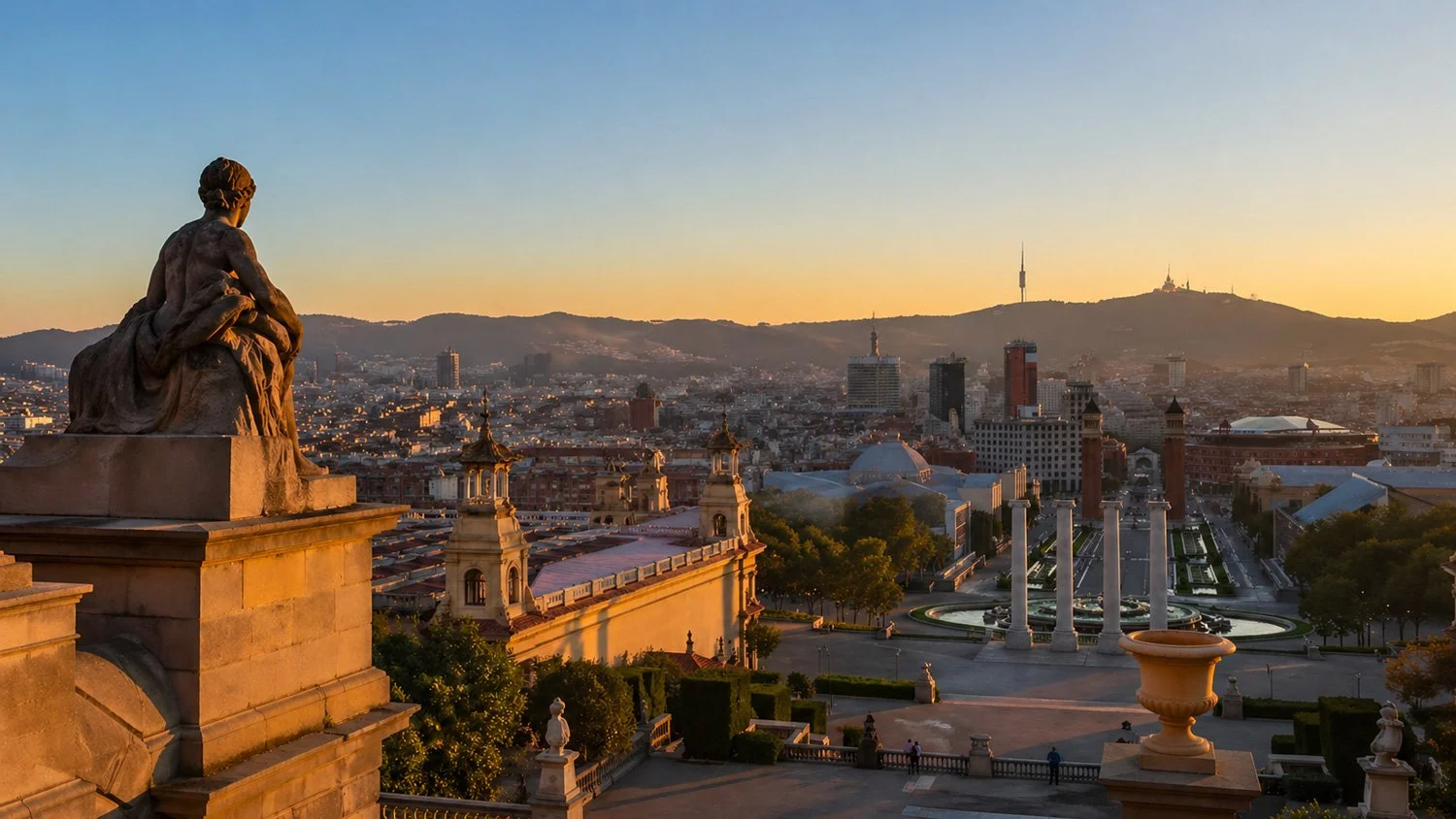 A cityscape view of Barcelona at sunset, with a statue in the foreground and the Montjuïc hill with antenna in the background.