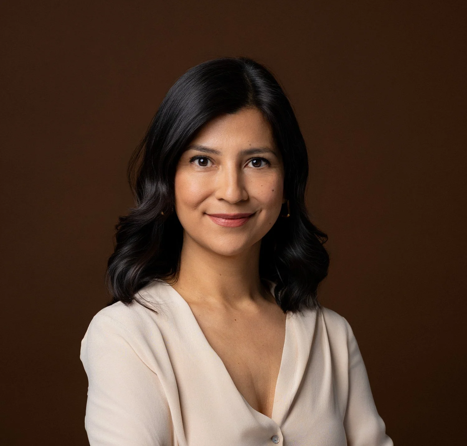Adriana Betancourt Paralegal at Altamare. Photo of a woman with shoulder-length black hair, wearing a light-colored blouse, smiling against a plain brown background.