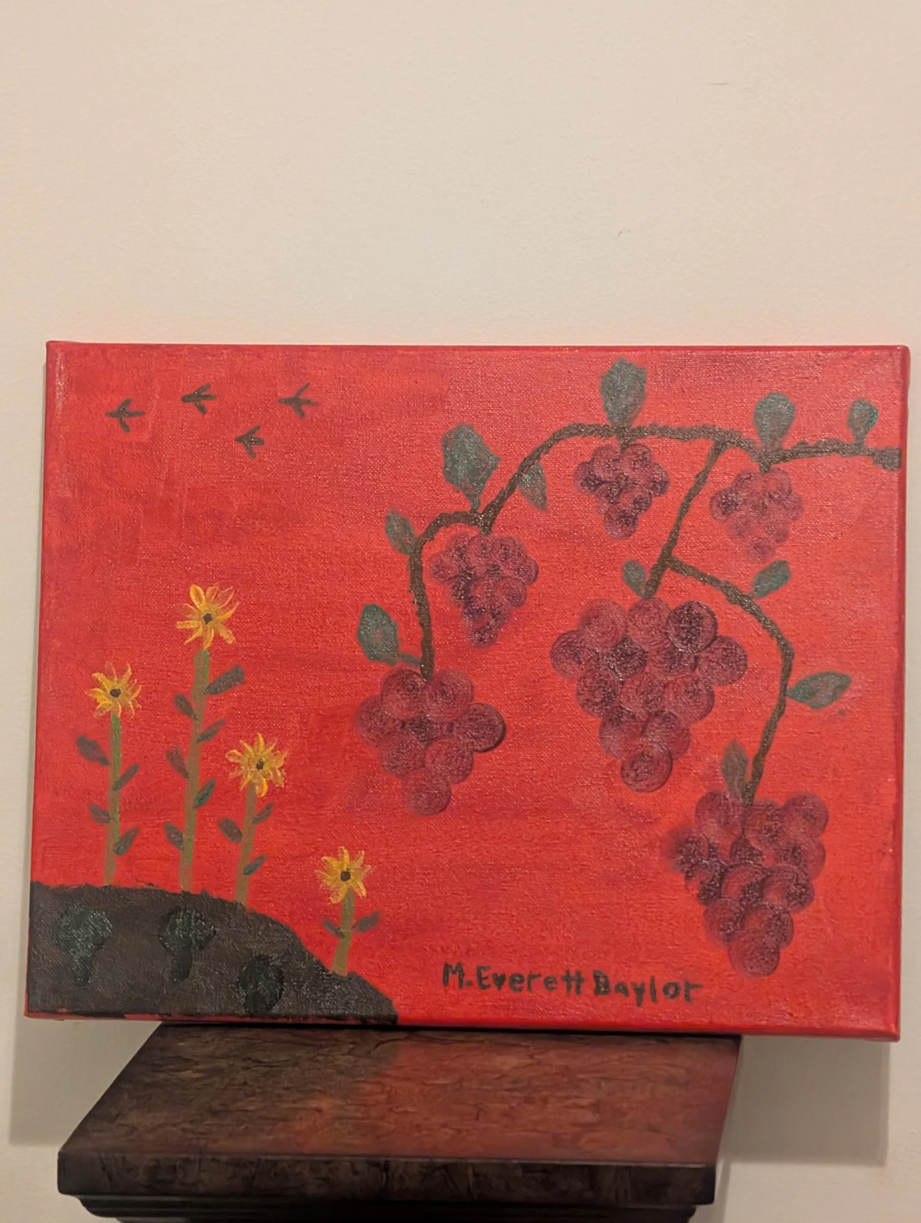 Painting of red grapes hanging from a vine with a red background, yellow flowers in the bottom left corner, and black birds flying in the sky. Signed 'M. Everett Baylor' at the bottom.
