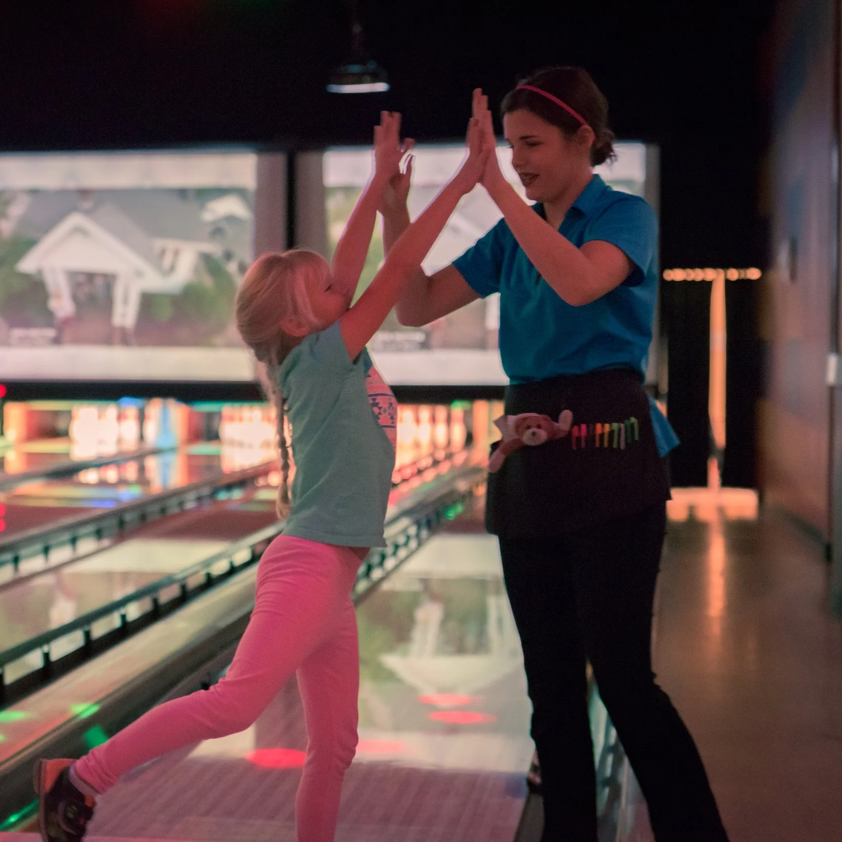 A young girl and a female bowling alley employee giving each other a high five in a bowling alley.