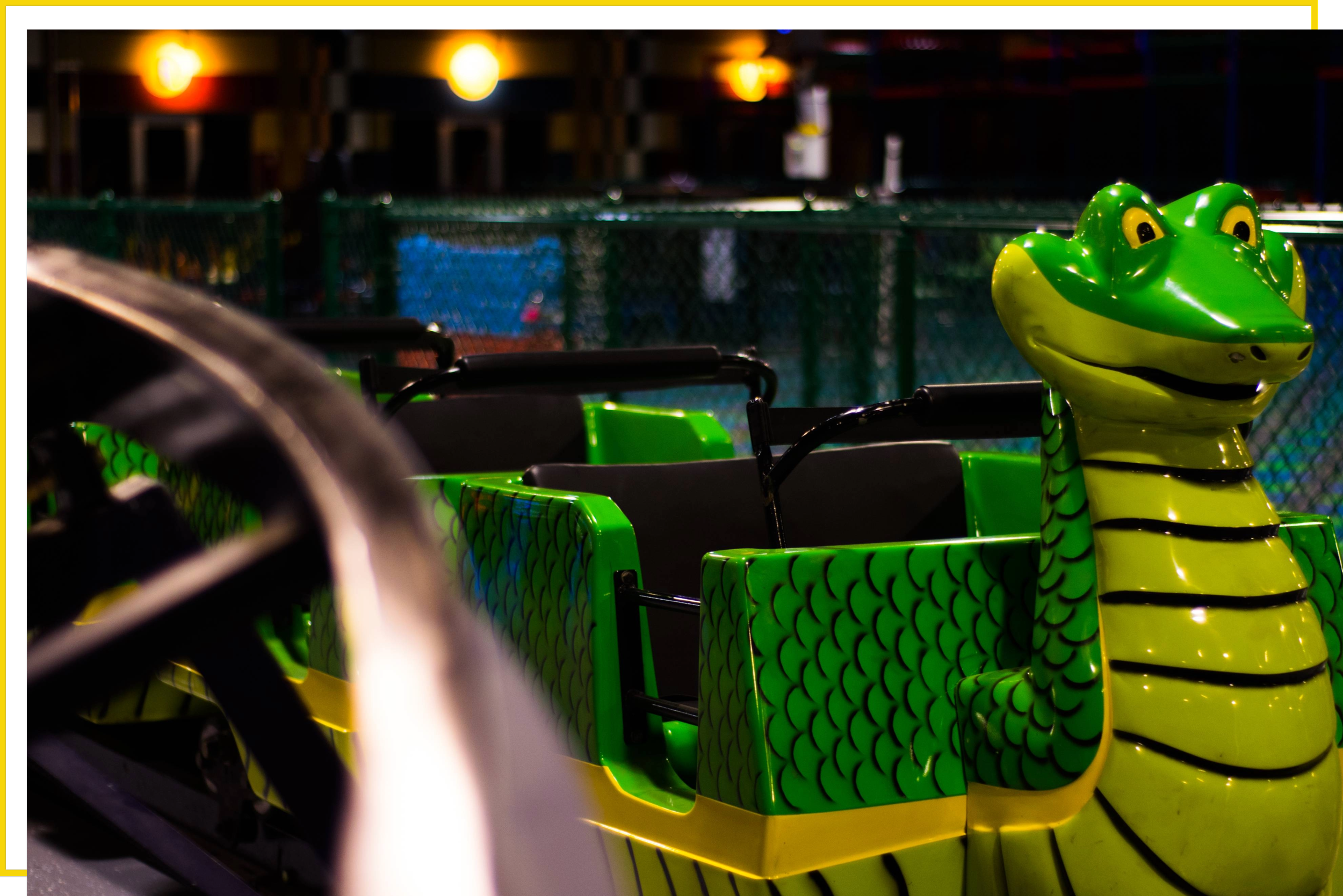 Northwest Arkansas' only indoor roller coaster. An amusement park ride featuring a green and yellow crocodile-shaped vehicle with a smiling face, black stripes, and a scale pattern on the sides.