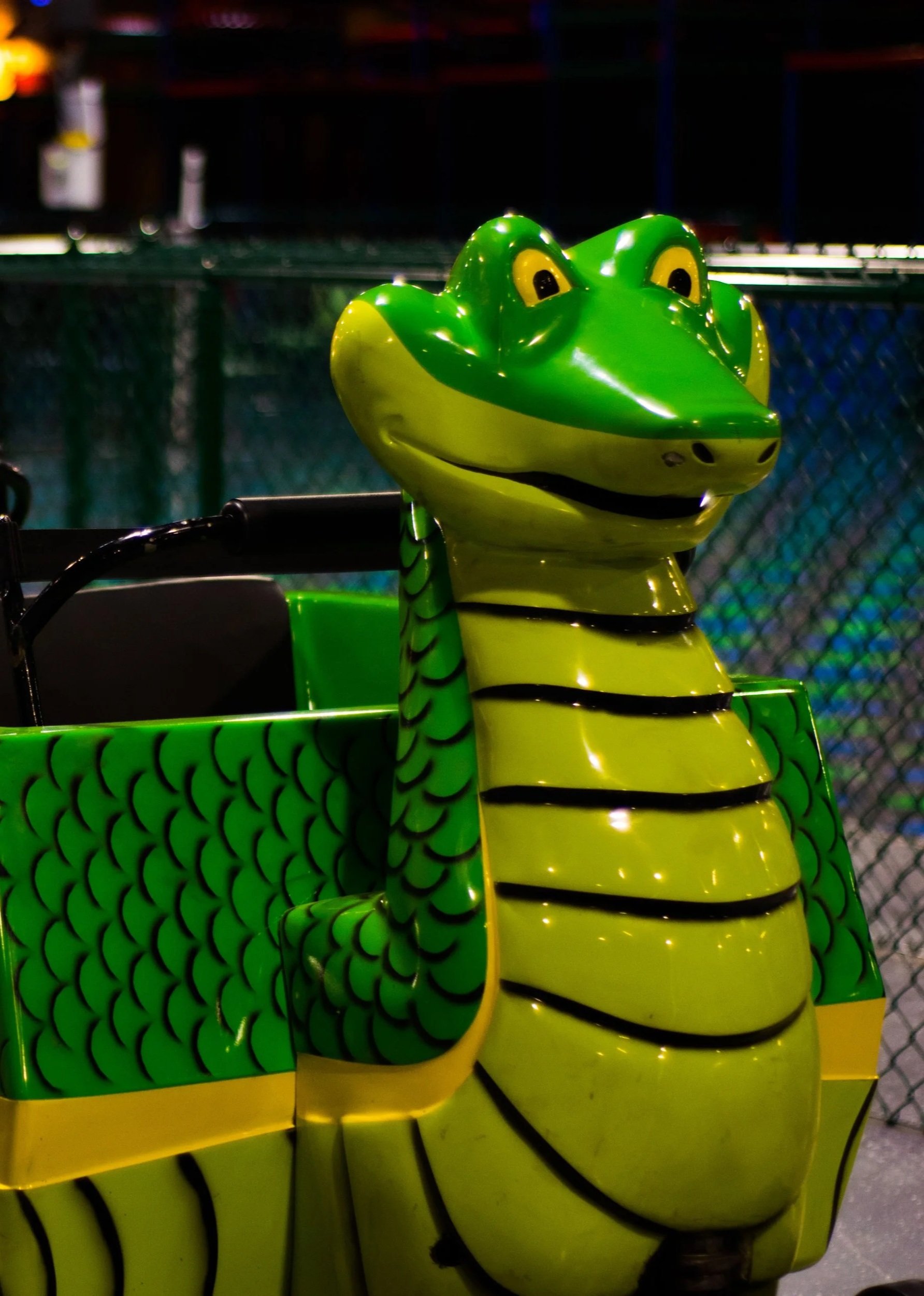 A green and yellow cartoon alligator figure with a smiling face, missing a nose, and black stripes, part of a carnival ride.