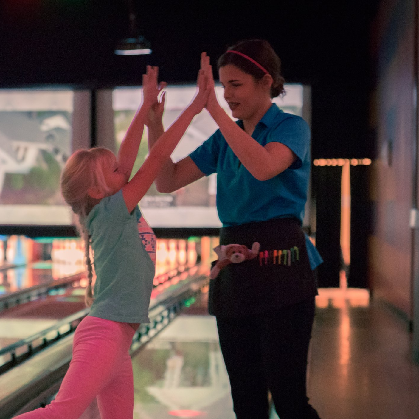 A young girl and a bowling alley employee high-fiving at the bowling alley.