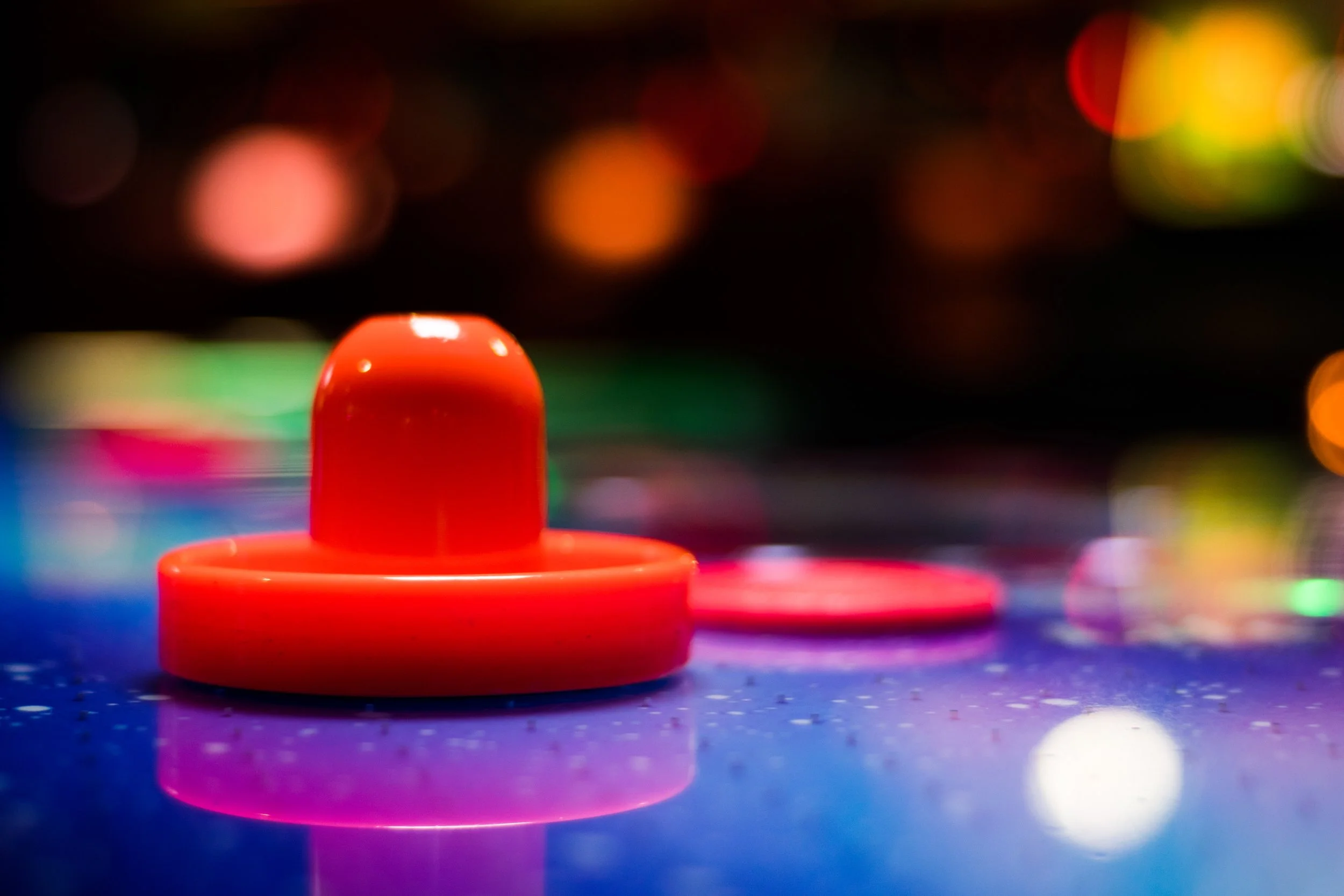 Close-up of a red game piece on a blue game board with colorful blurred lights in the background.