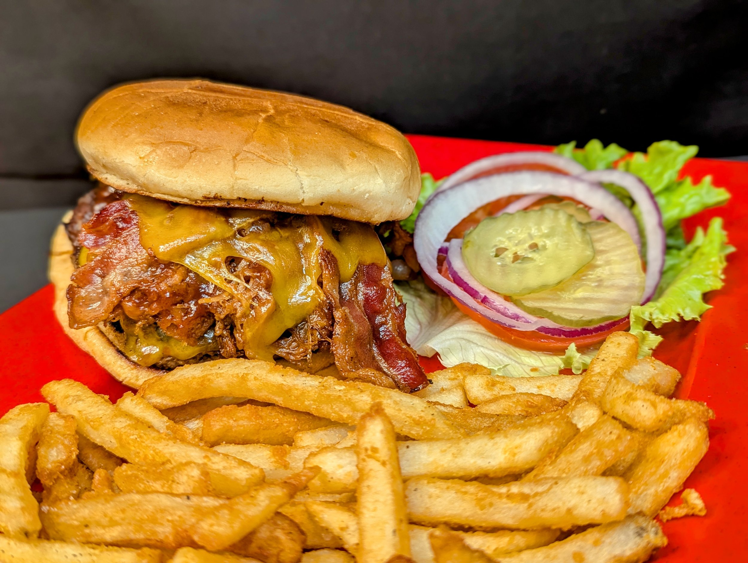 Cheeseburger with bacon, lettuce, tomato, pickles, onions, and French fries alongside a side salad with onion, tomato, and cucumber slices.