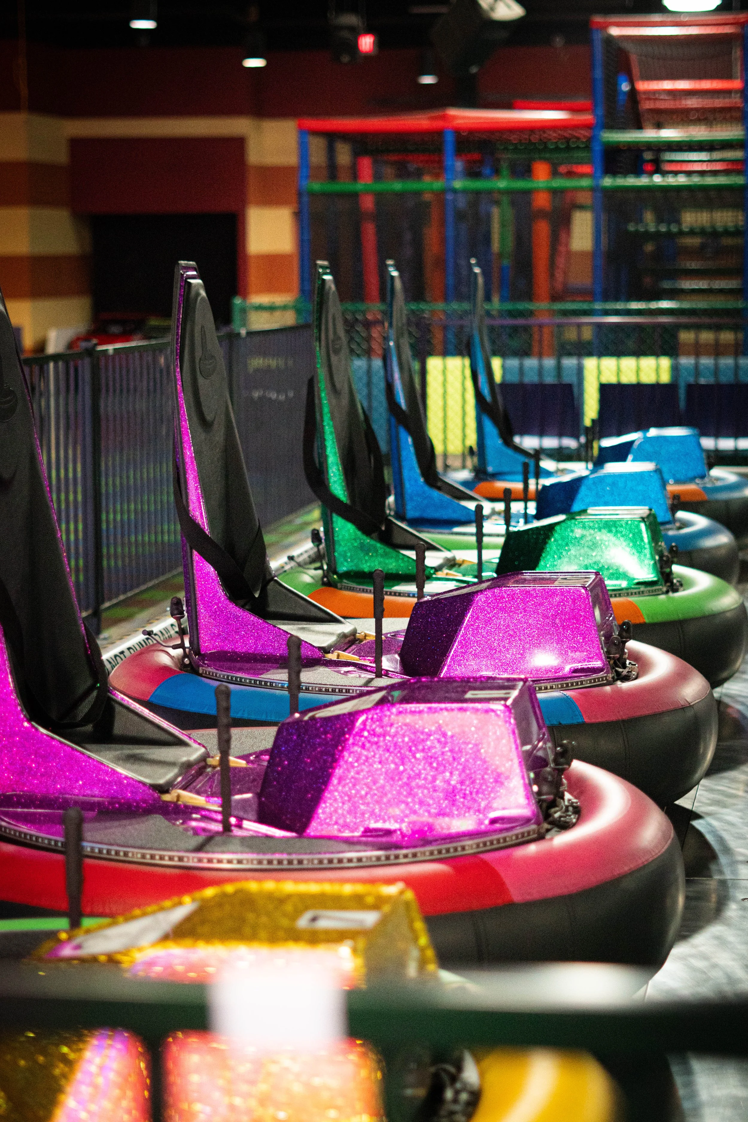 Colorful bumper cars with glittery surfaces in an amusement park, arranged in a row.
