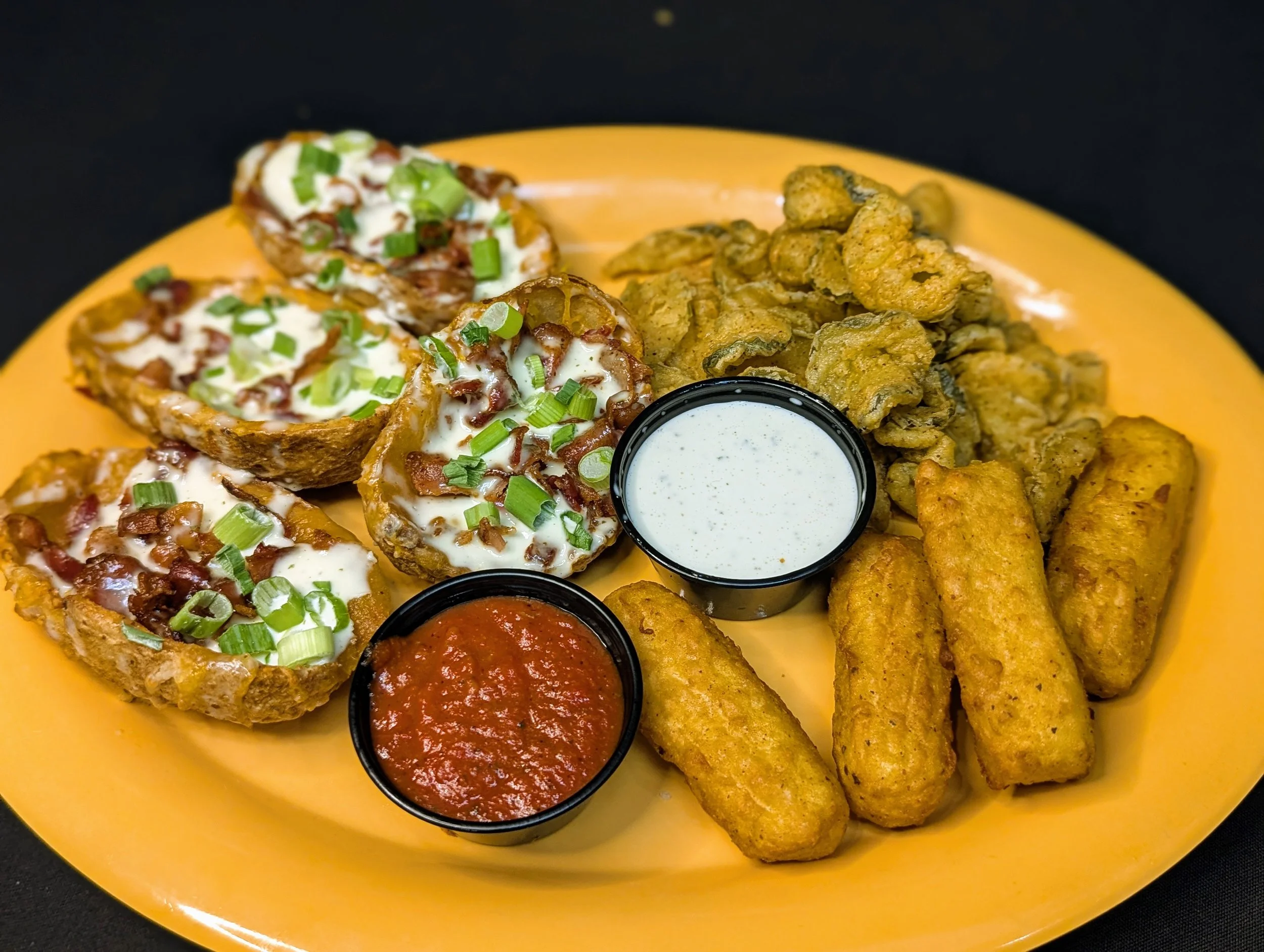 Appetizer platter with stuffed baked potatoes topped with cheese, bacon, and green onions, fried fish fillets, fried onion rings, and two small cups of dipping sauces, sour cream and marinara.