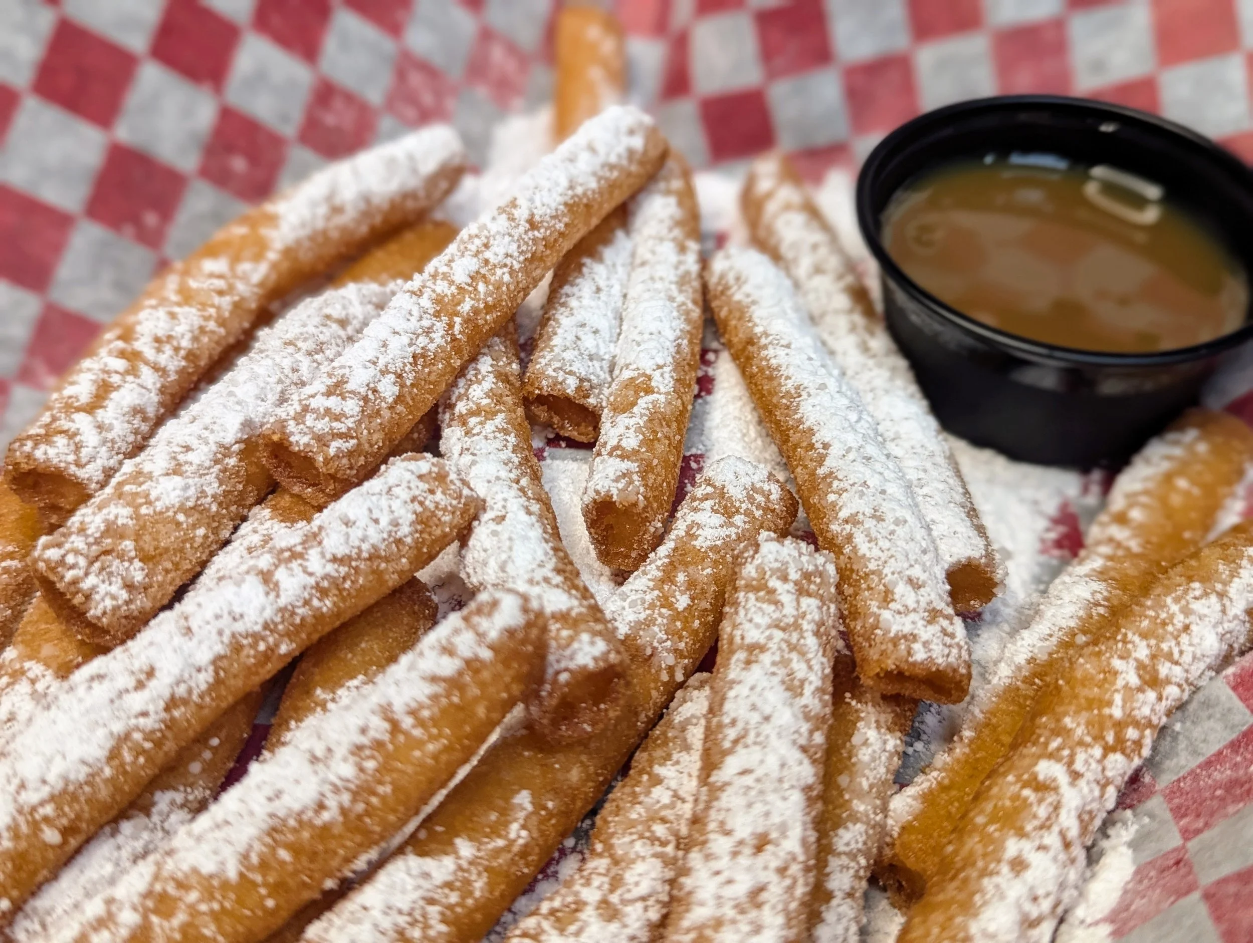 Plate of crispy fried mozzarella sticks dusted with powdered sugar and served with a side of dipping sauce.