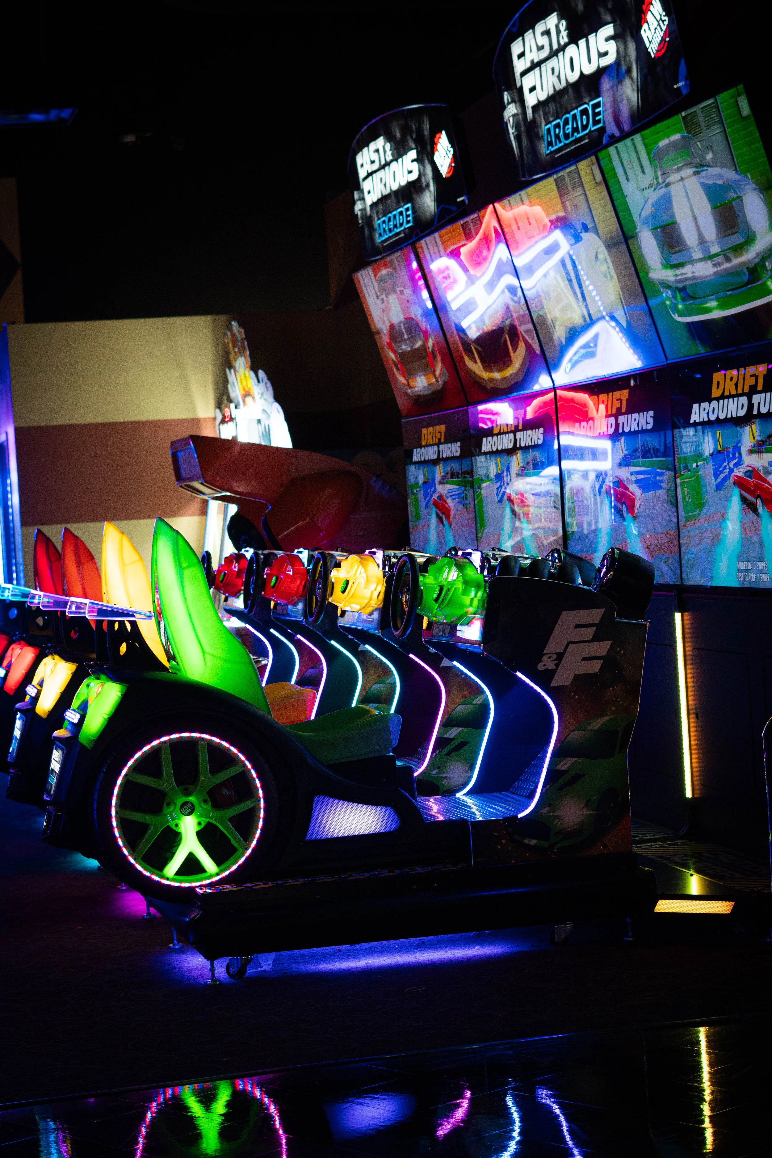 Colorful indoor arcade with racing game pods and large screens displaying car racing animations.