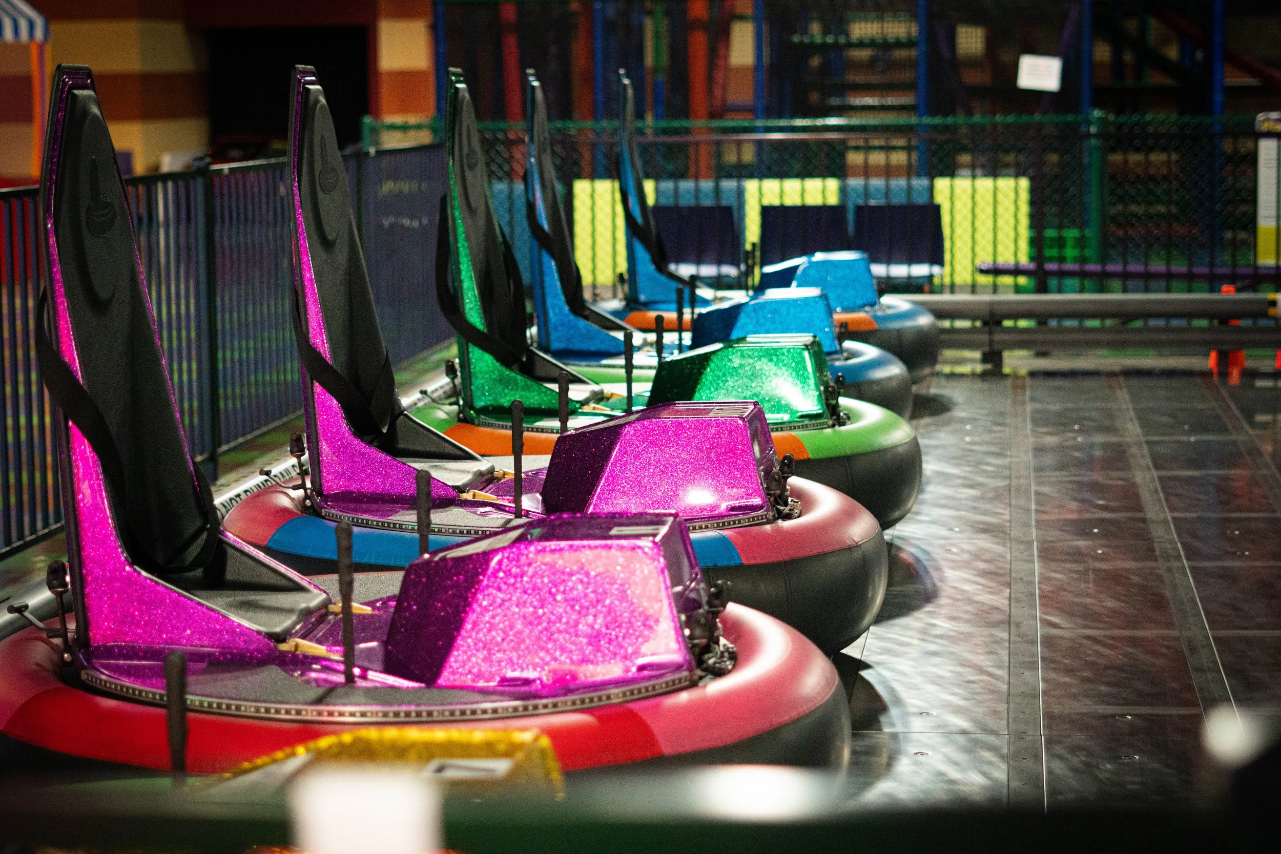Colorful bumper cars in an amusement park ride, lined up in a row inside a safety barrier.